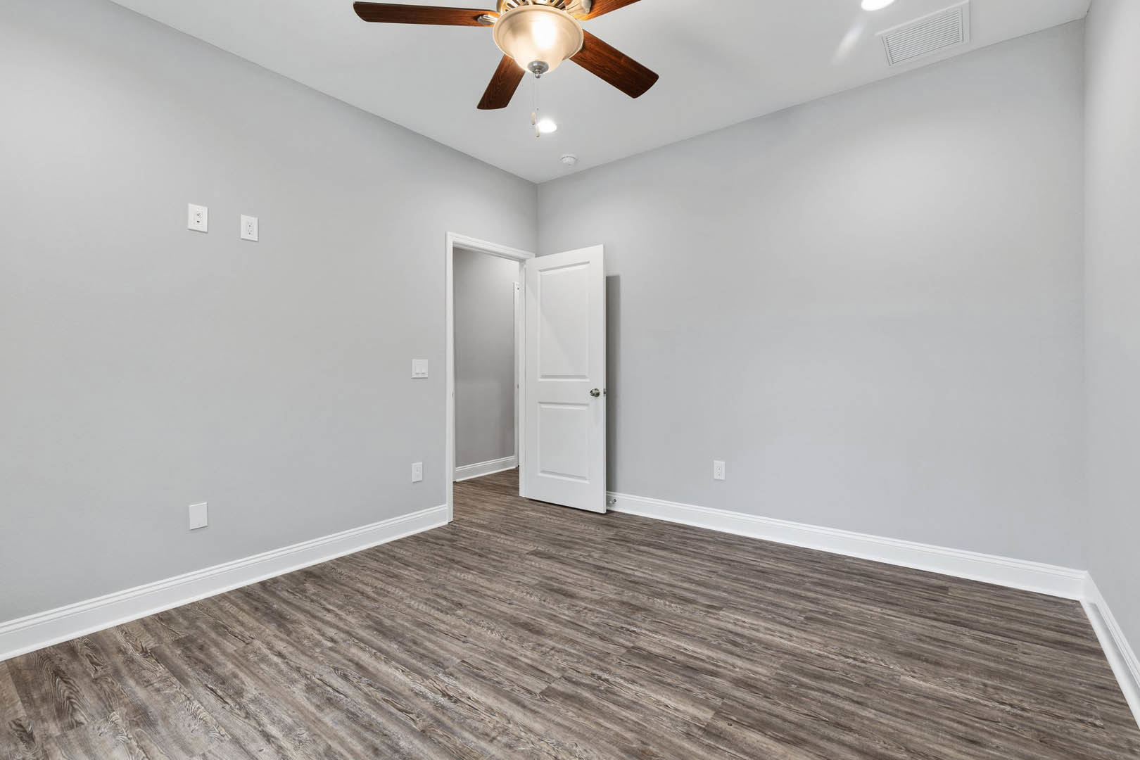 Wood flooring, white paneled door with silver knob, ceiling fan with light fixture, smooth white walls and ceiling