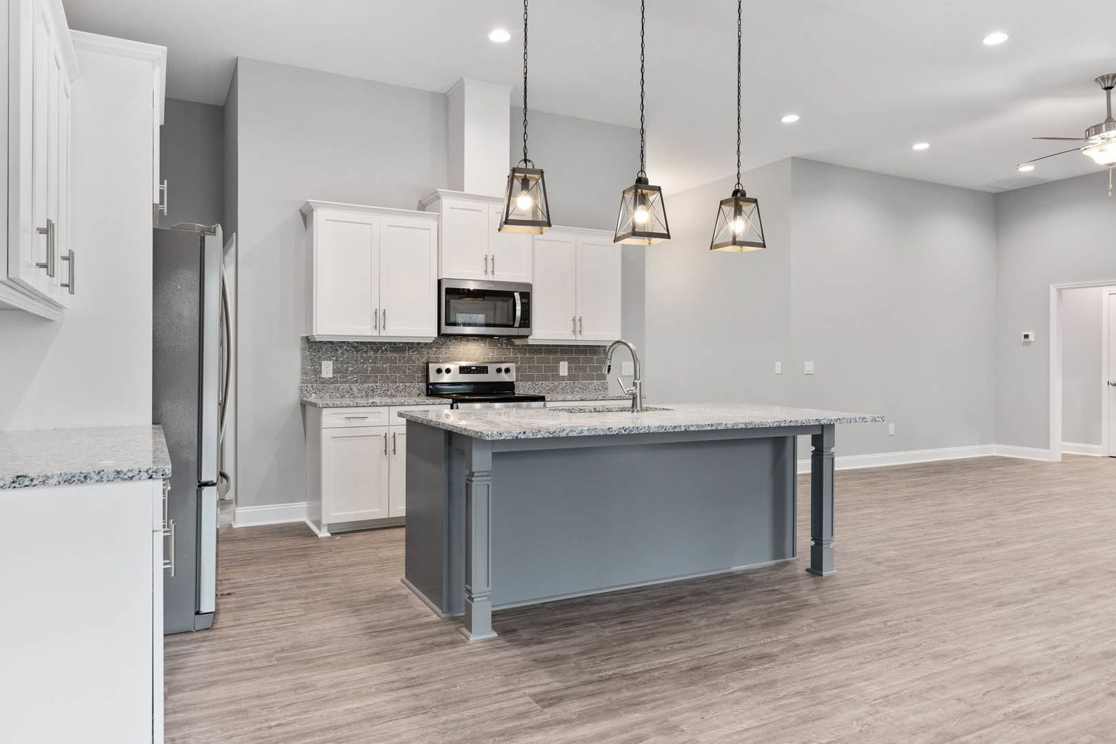 Spacious kitchen featuring a large central island with stone countertop, stainless steel refrigerator, wood flooring, white cabinetry, built-in microwave, and modern square-framed