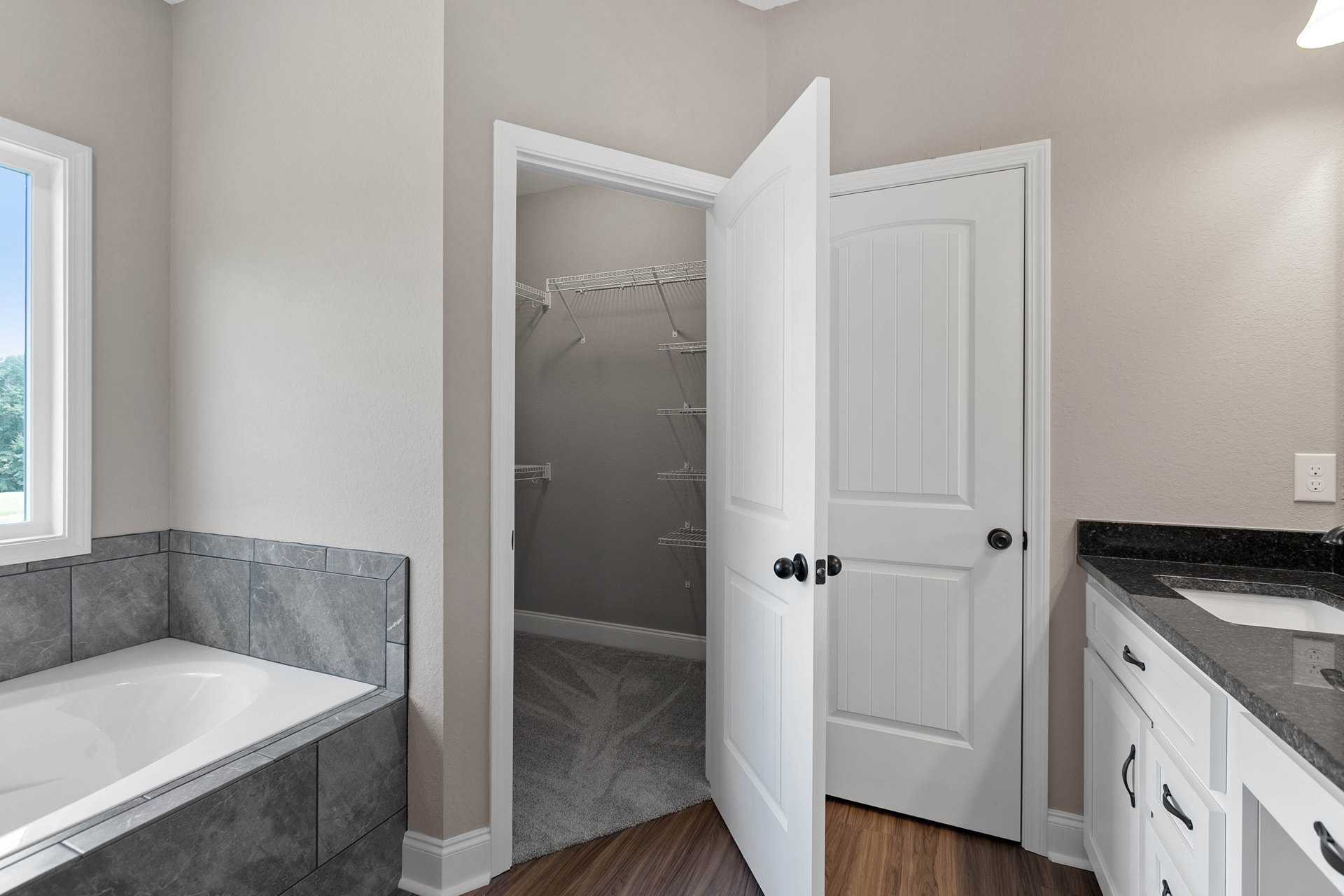 Walk-in closet with built-in shelving, freestanding white bathtub, tile flooring, white door with black hardware, and window providing natural light