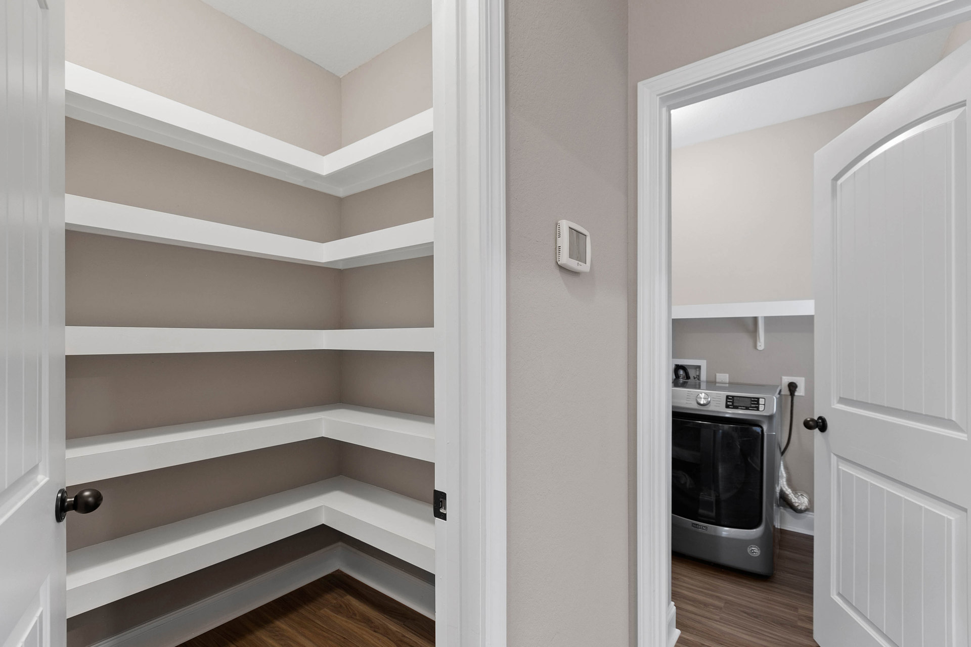 Laundry room with built-in white shelves, white cabinetry, and a front-loading dryer; white door with black handles and visible wall molding