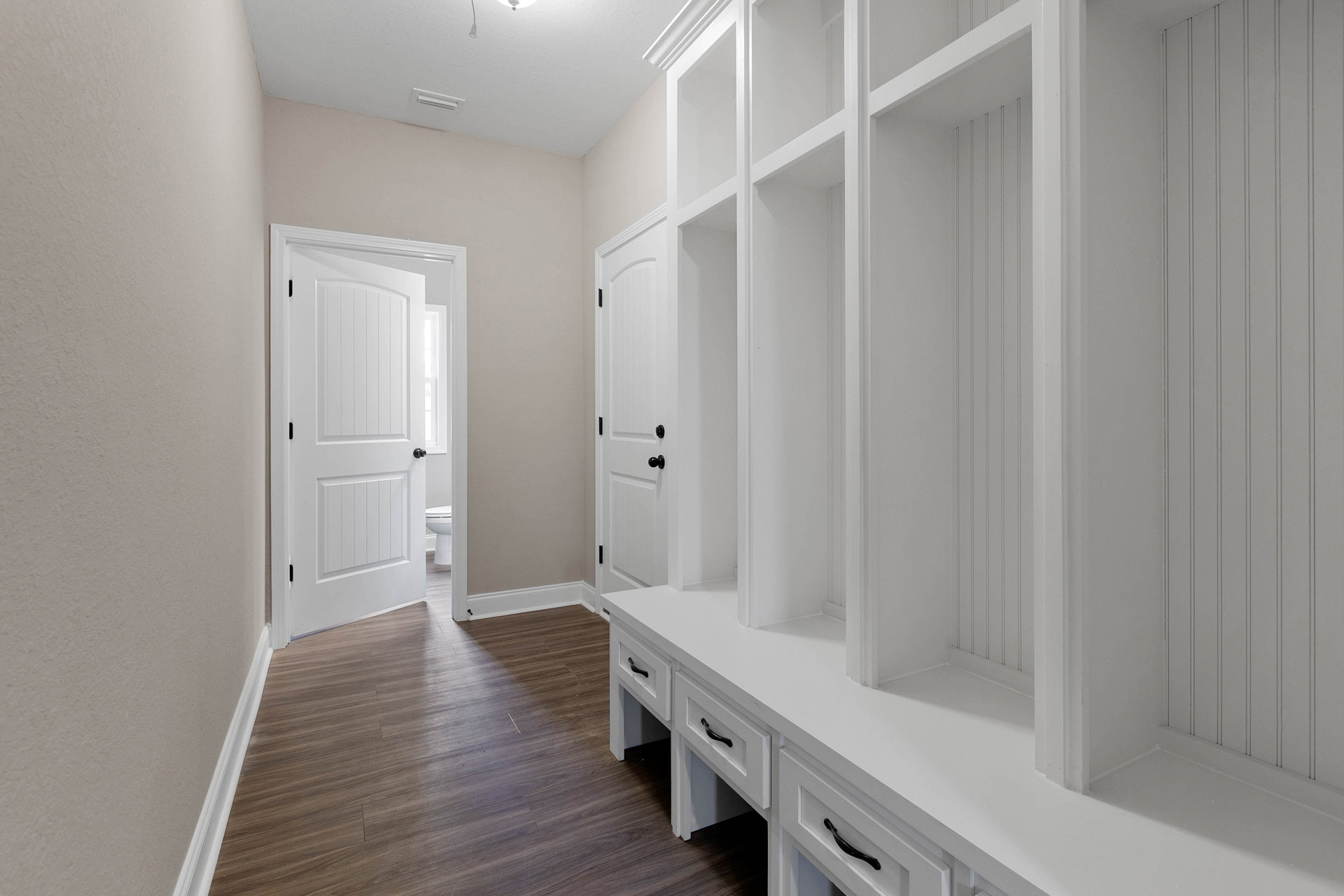 Hallway with built-in white shelves, wood flooring, white door with black knobs, and white trim