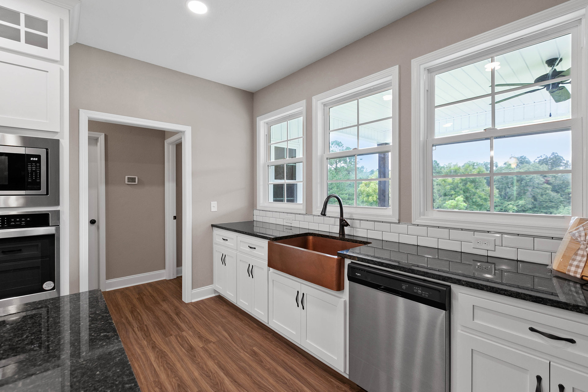 White kitchen cabinets with black countertops, copper sink set in marble, stainless steel oven and microwave, dishwasher with black handle, plastic-wrapped bow on counter