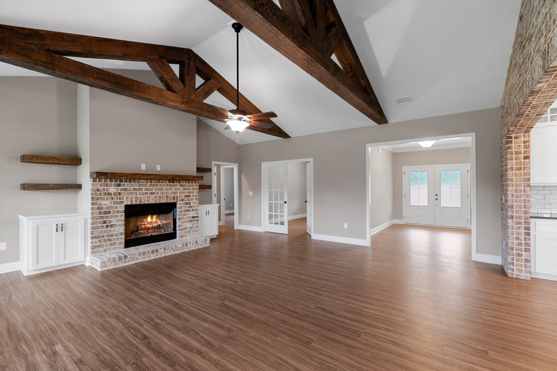 Living room featuring hardwood floors, white trim, a lit fireplace with white mantel, double glass-paneled doors, and white cabinetry with black handles
