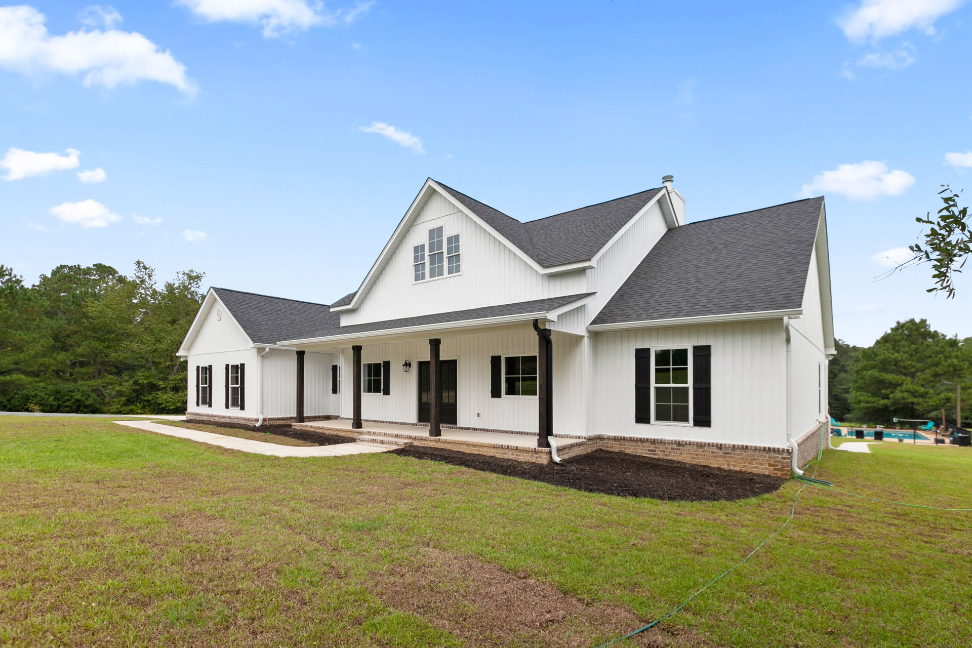 White house with black shutters, covered porch, manicured lawn, blue sky, and Robert Frost Farm visible in the background, surrounded by trees and bushes.