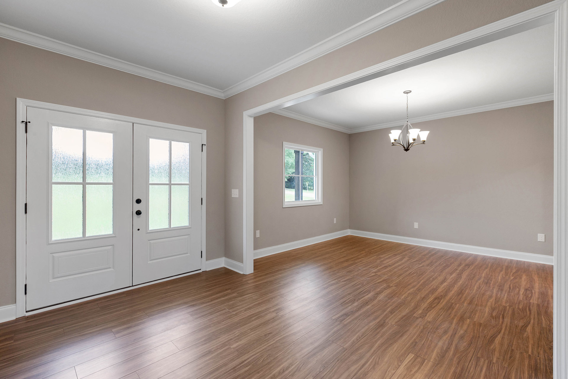 Wood flooring with white trim, double white doors featuring frosted glass panels, window with white frame, chandelier with white shades, neutral walls and ceiling