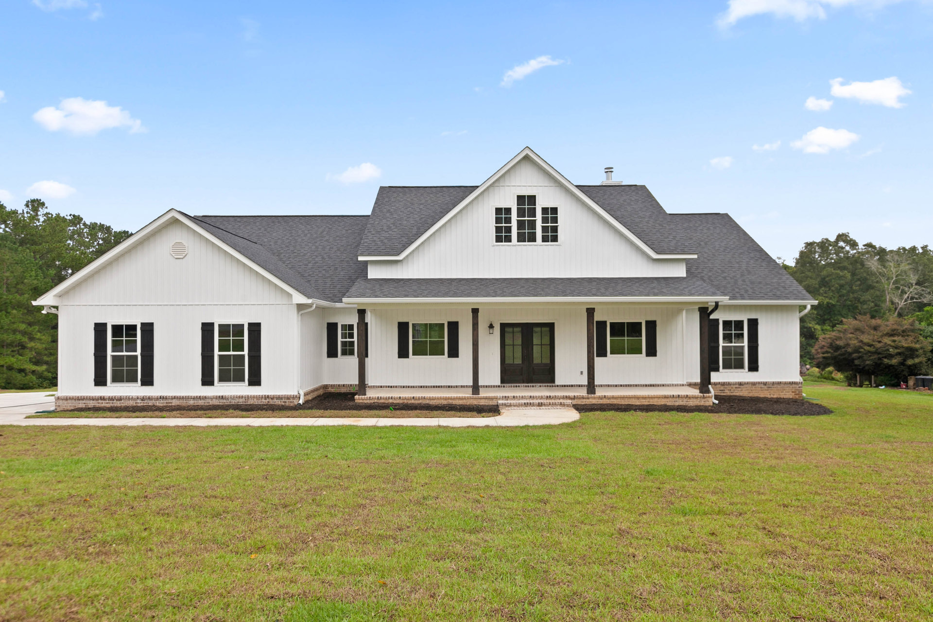 White house with black shutters and double glass-paneled front doors, surrounded by a green lawn and walkway, Robert Frost Farm visible in the background under a partly cloudy sky.