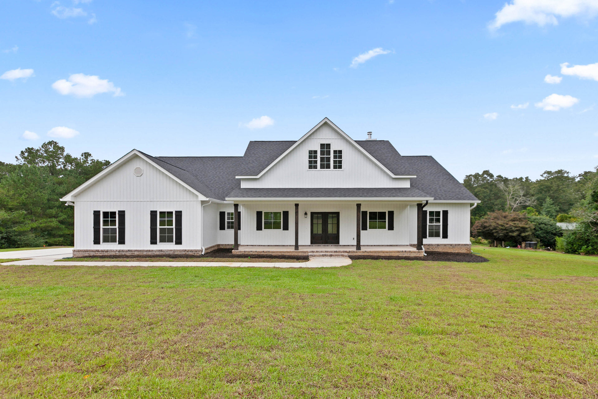 White house with black shutters, double glass-paneled doors, white-framed windows, manicured lawn, walkway, and Robert Frost Farm visible in the background under a blue sky.