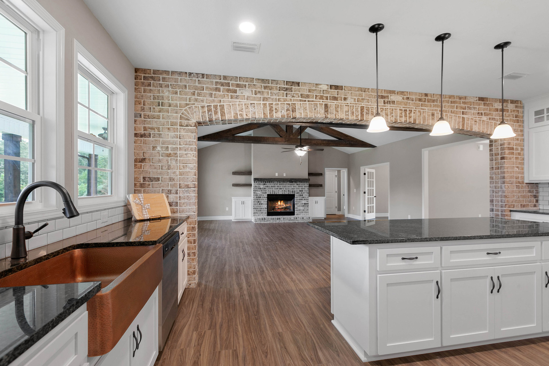 Kitchen with exposed brick wall, lit fireplace, white island with black countertops, stainless steel faucet, cabinetry, and metal pole with red stripe and sign