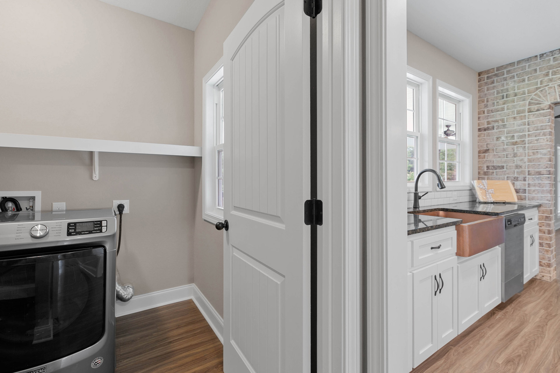 White-paneled door with black hardware set in a kitchen featuring wood flooring, white baseboards, and stainless steel stove adjacent to white cabinetry and light-colored