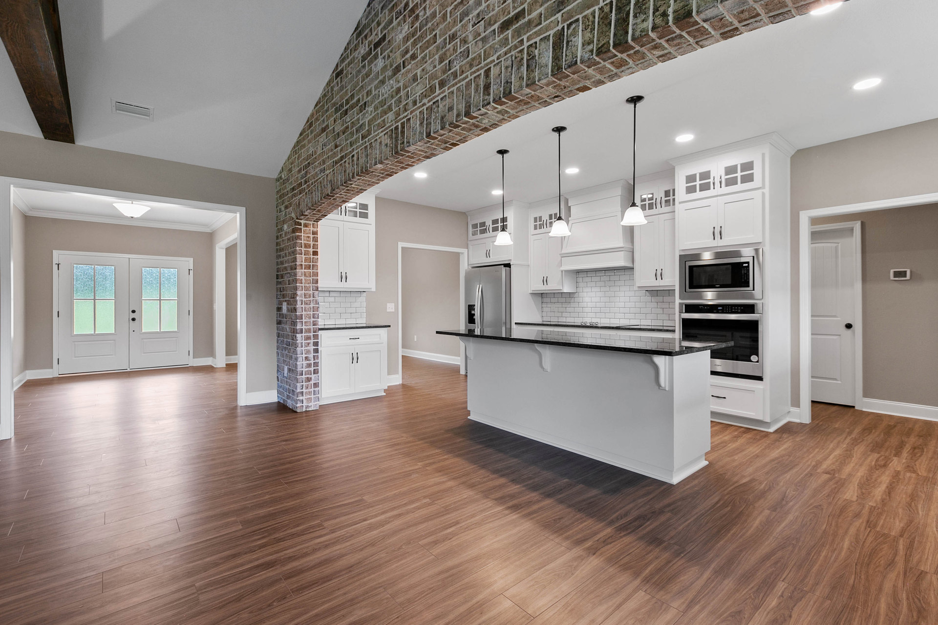 Kitchen featuring exposed brick wall, large central island with white base and black countertop, wood flooring, cabinetry, built-in microwave, double doors with frosted glass