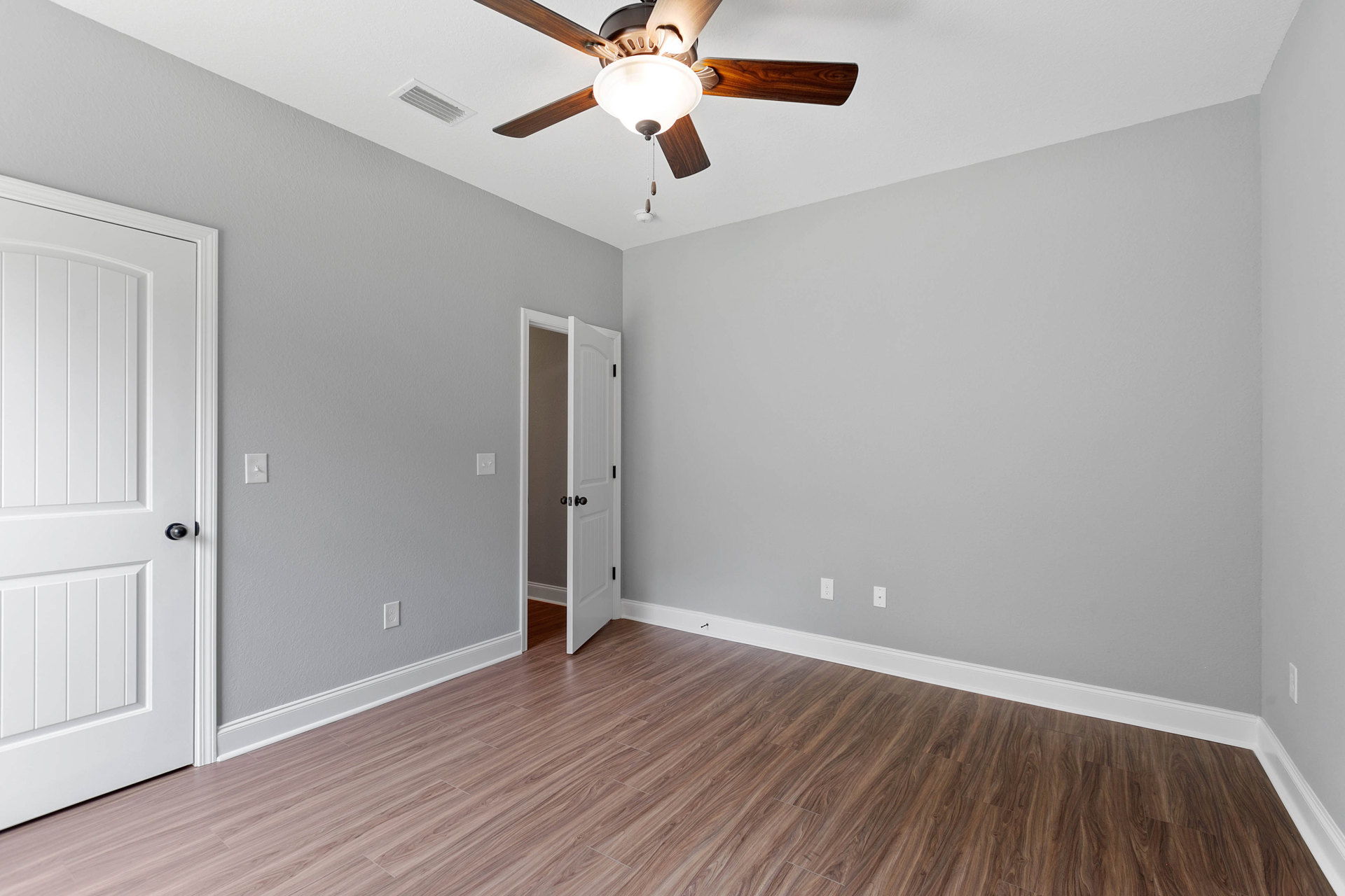 Ceiling fan with light fixture mounted on white ceiling above wood flooring, white door with silver doorknob visible on adjacent wall