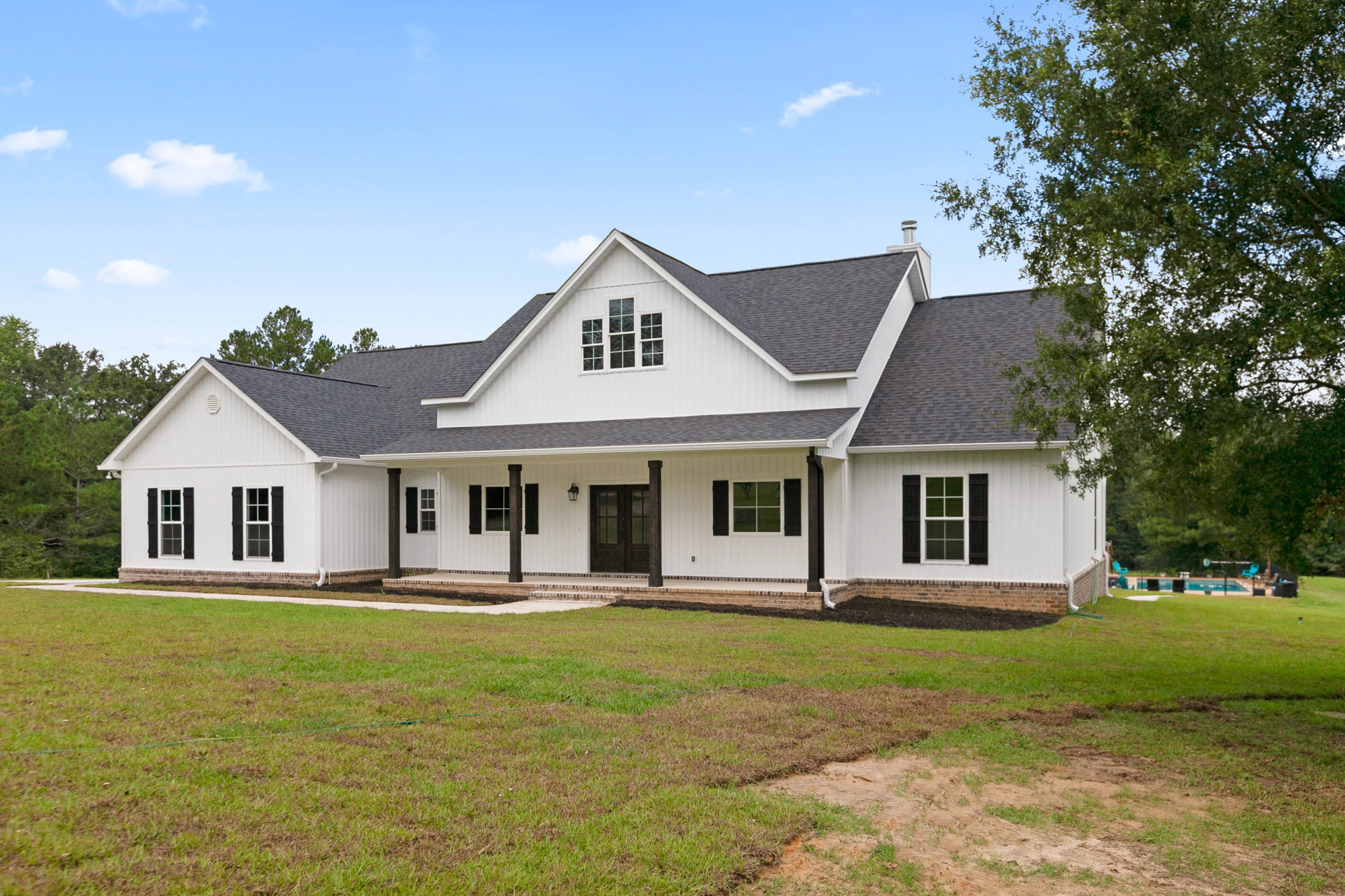White house with black-trimmed windows, double glass-paneled front doors, and a manicured lawn; tree beside the house and Robert Frost Farm visible in the background.
