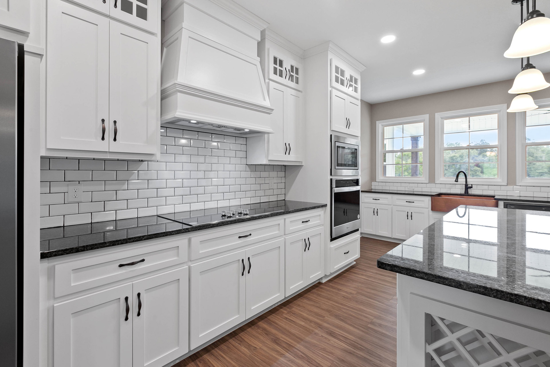 Kitchen featuring white shaker cabinets with black countertops, marble island, stainless steel appliances, glass door, and black cabinet handles
