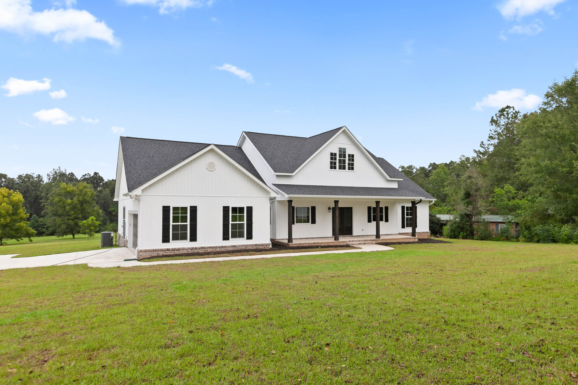 White house with black shutters and covered porch, manicured green lawn in foreground, Robert Frost Farm visible in background, blue sky with scattered clouds