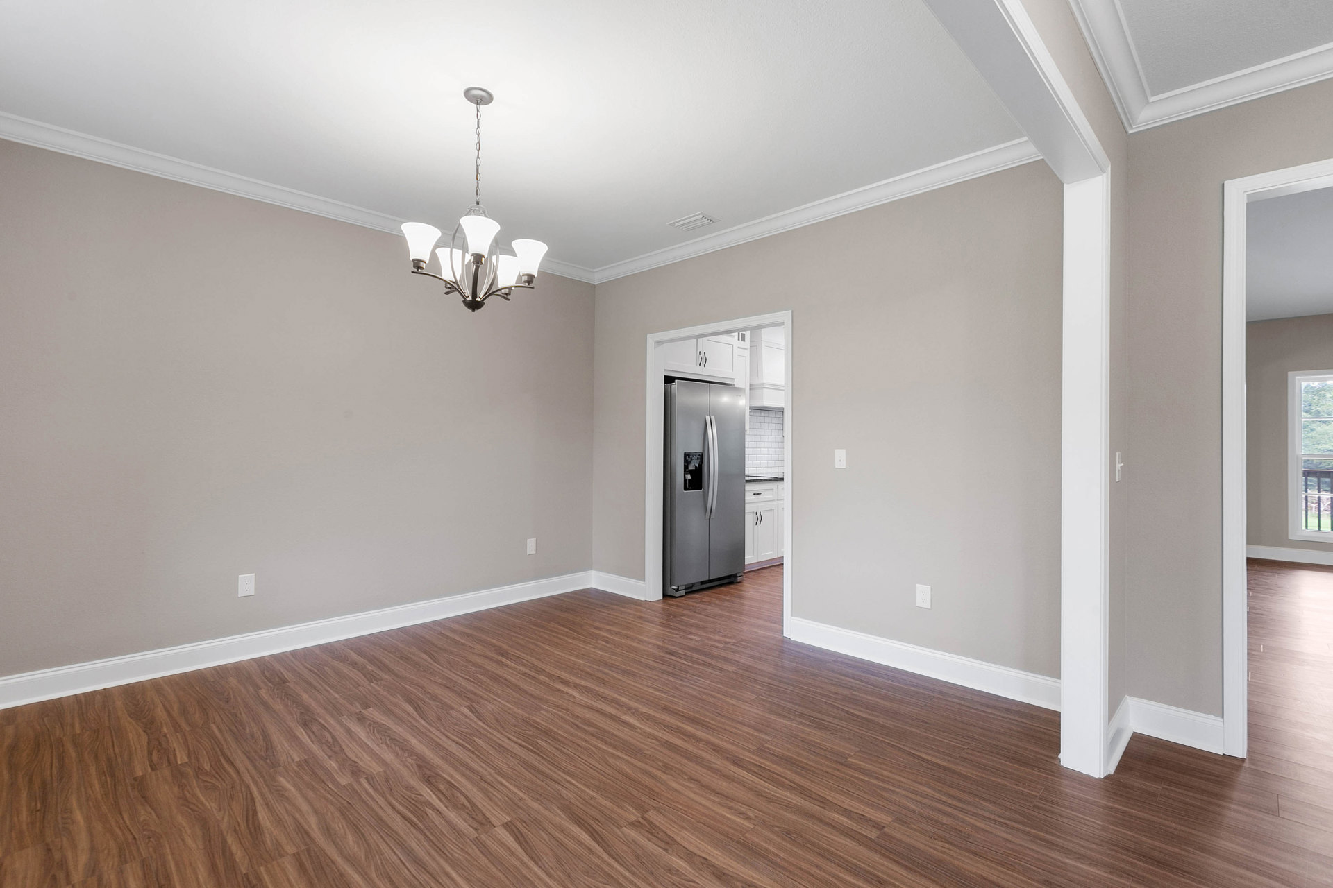 Open-concept room with light wood flooring, modern chandelier, stainless steel refrigerator, large window overlooking trees, and plaster ceiling