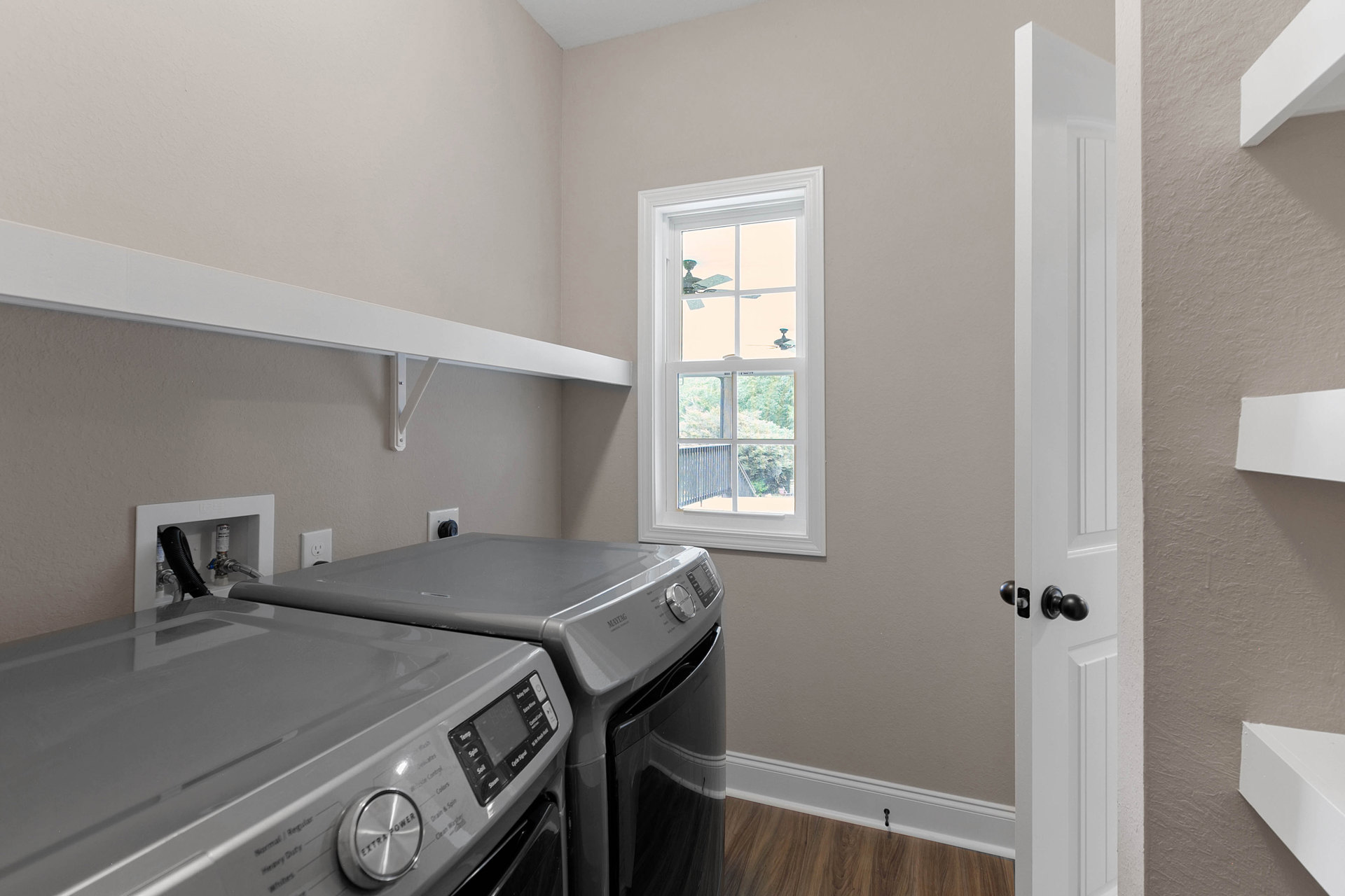 Front-loading washer and dryer set in a laundry room with white cabinetry, light-colored walls, and a window fitted with a fan.