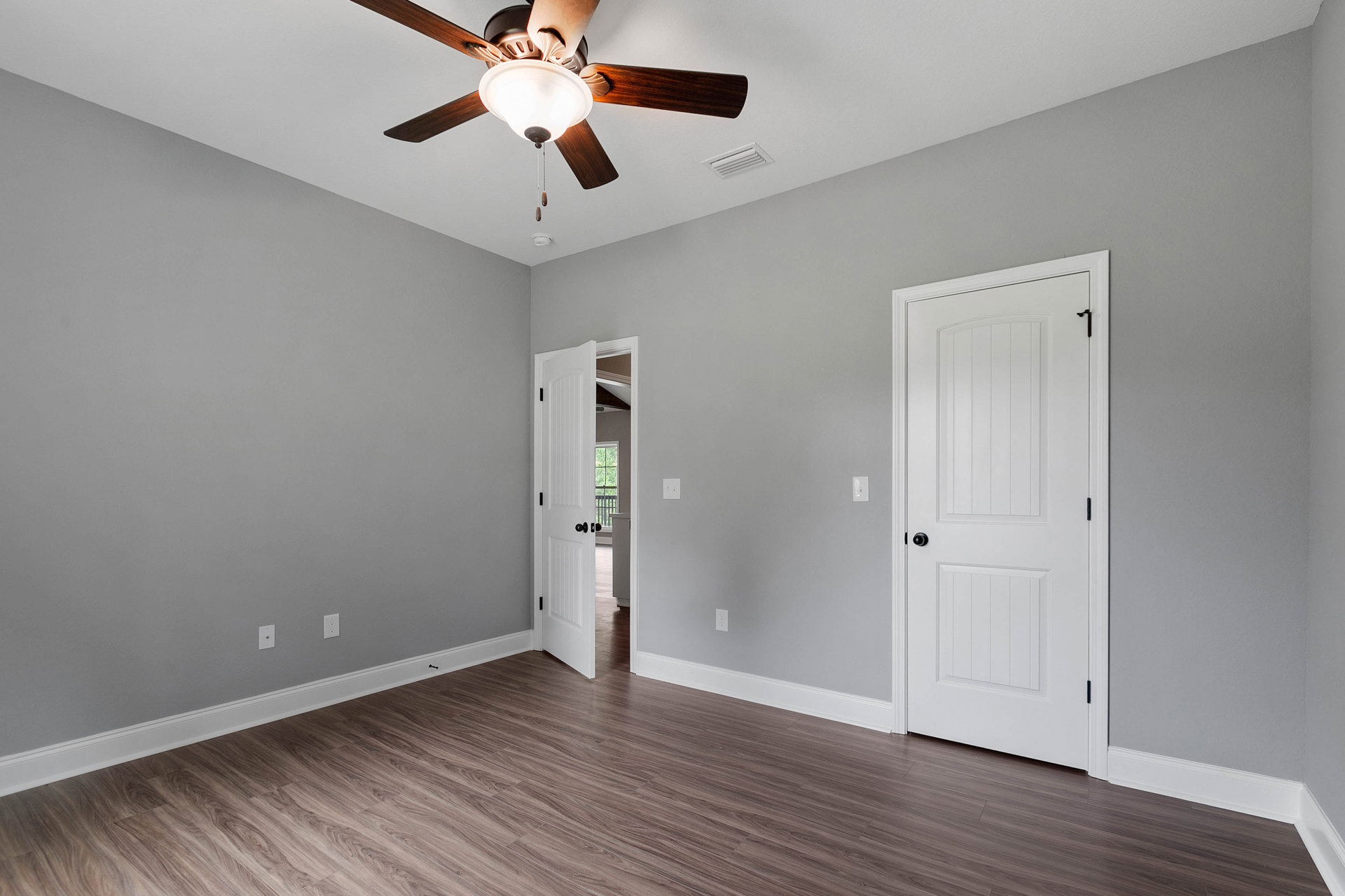 Ceiling fan with light fixture mounted above wood flooring, white walls, and an open white door with black hardware