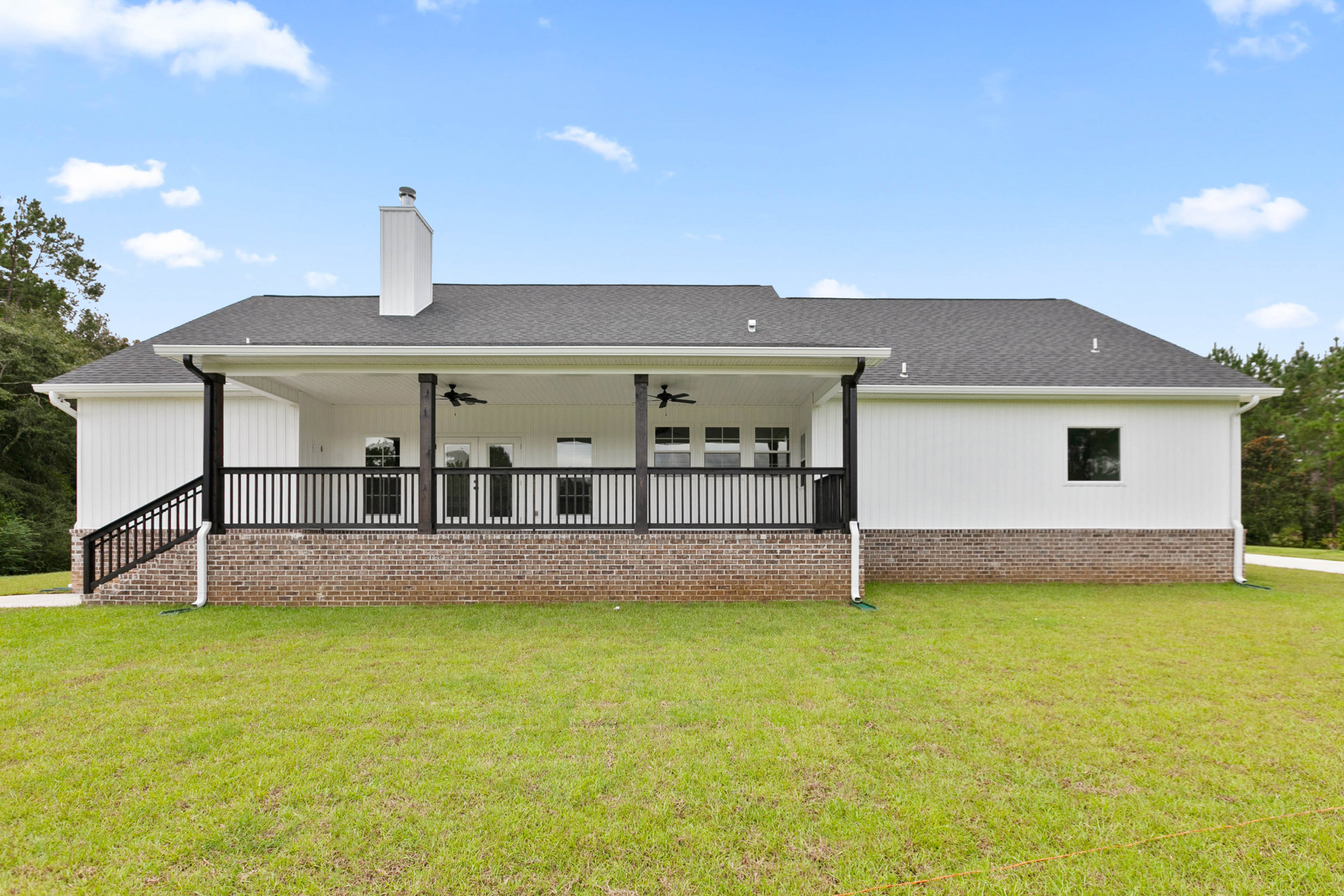 Brick house with covered porch, black metal railing, large windows, manicured lawn, and blue sky with scattered clouds