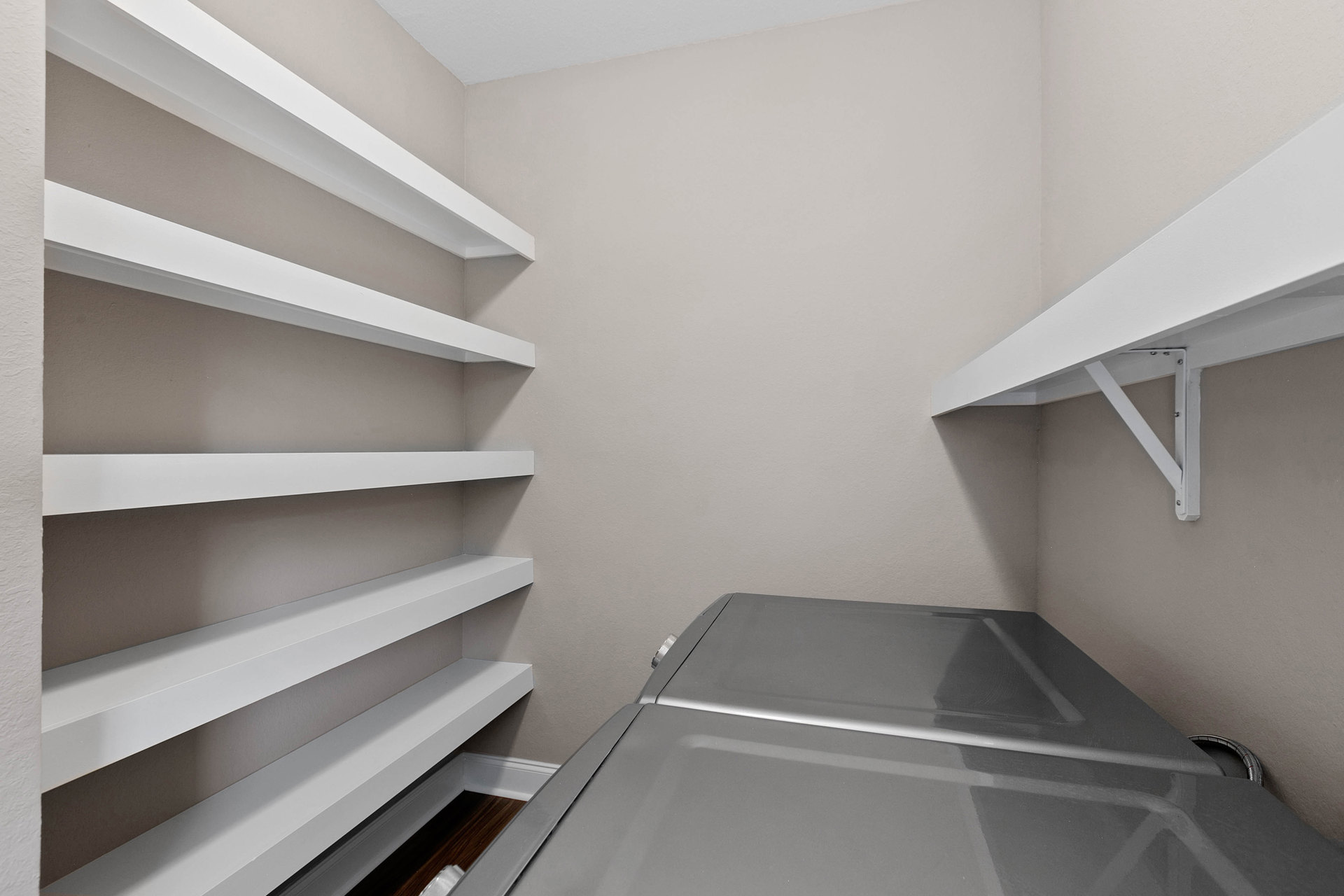 Built-in white shelves on a plaster wall above a stainless steel refrigerator in a modern kitchen interior