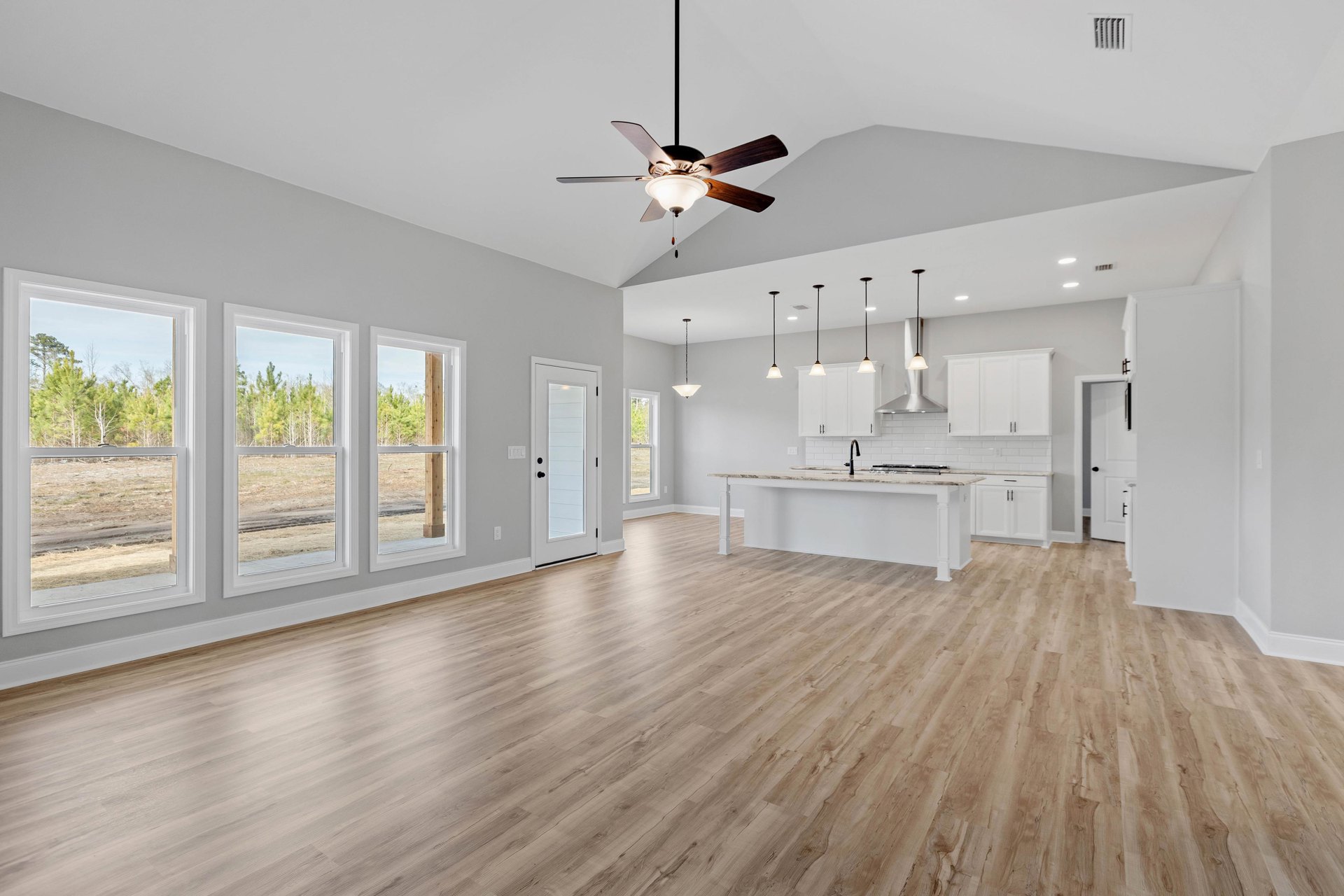 Open concept room with wood flooring, white walls, modern kitchen, ceiling fan with light, and white door featuring black hardware