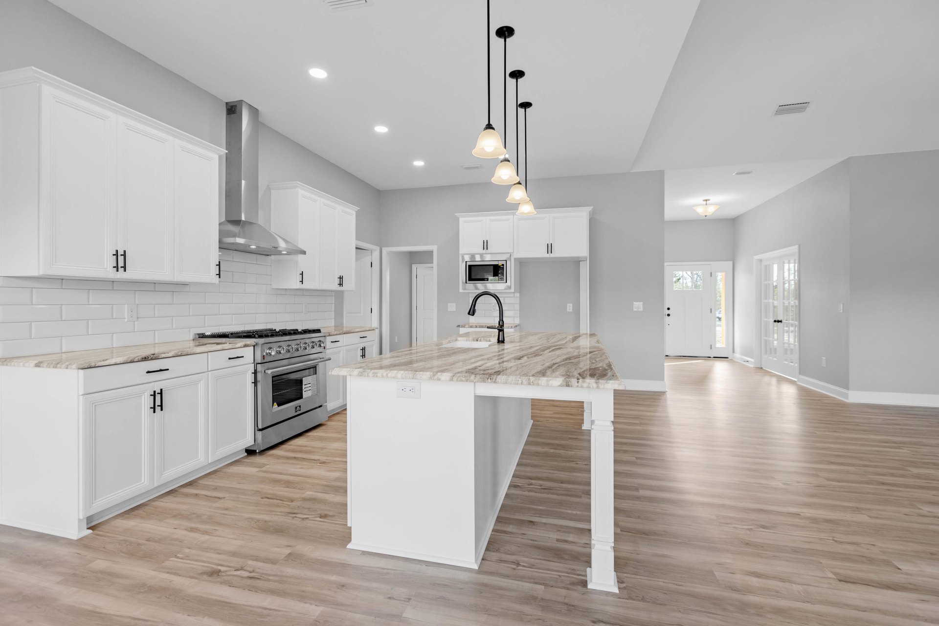 Marble kitchen island with black sink, stainless steel stove and microwave, pendant light, white cabinetry, hardwood flooring