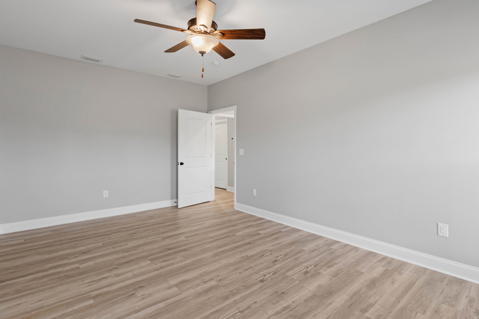Ceiling fan with light fixture above wood flooring, white door with black knob and wall thermostat, neutral walls and trim
