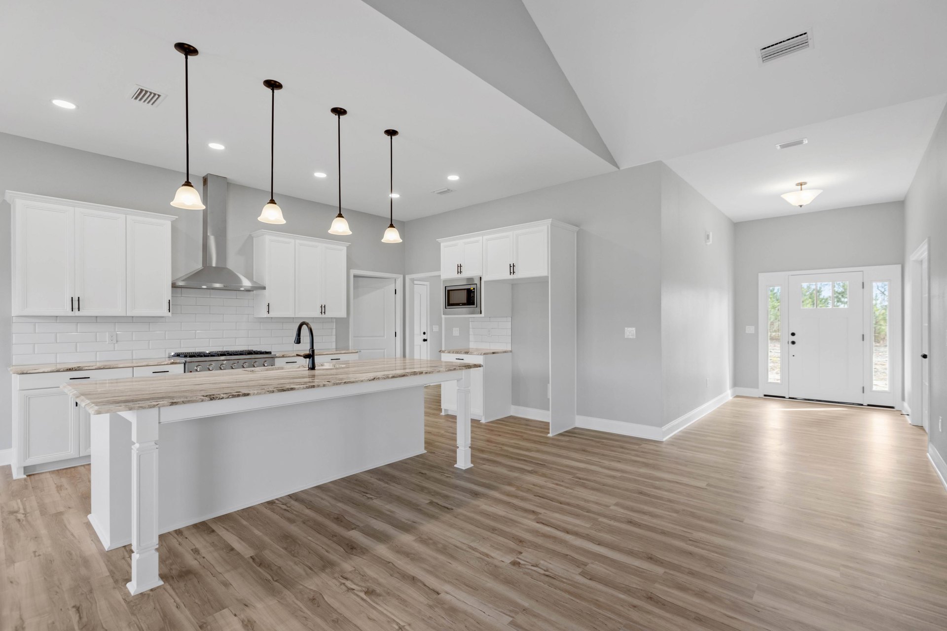 Open kitchen and dining area featuring marble countertops, tile flooring, white cabinetry, stainless steel sink, built-in microwave, white door with glass panes, and pendant