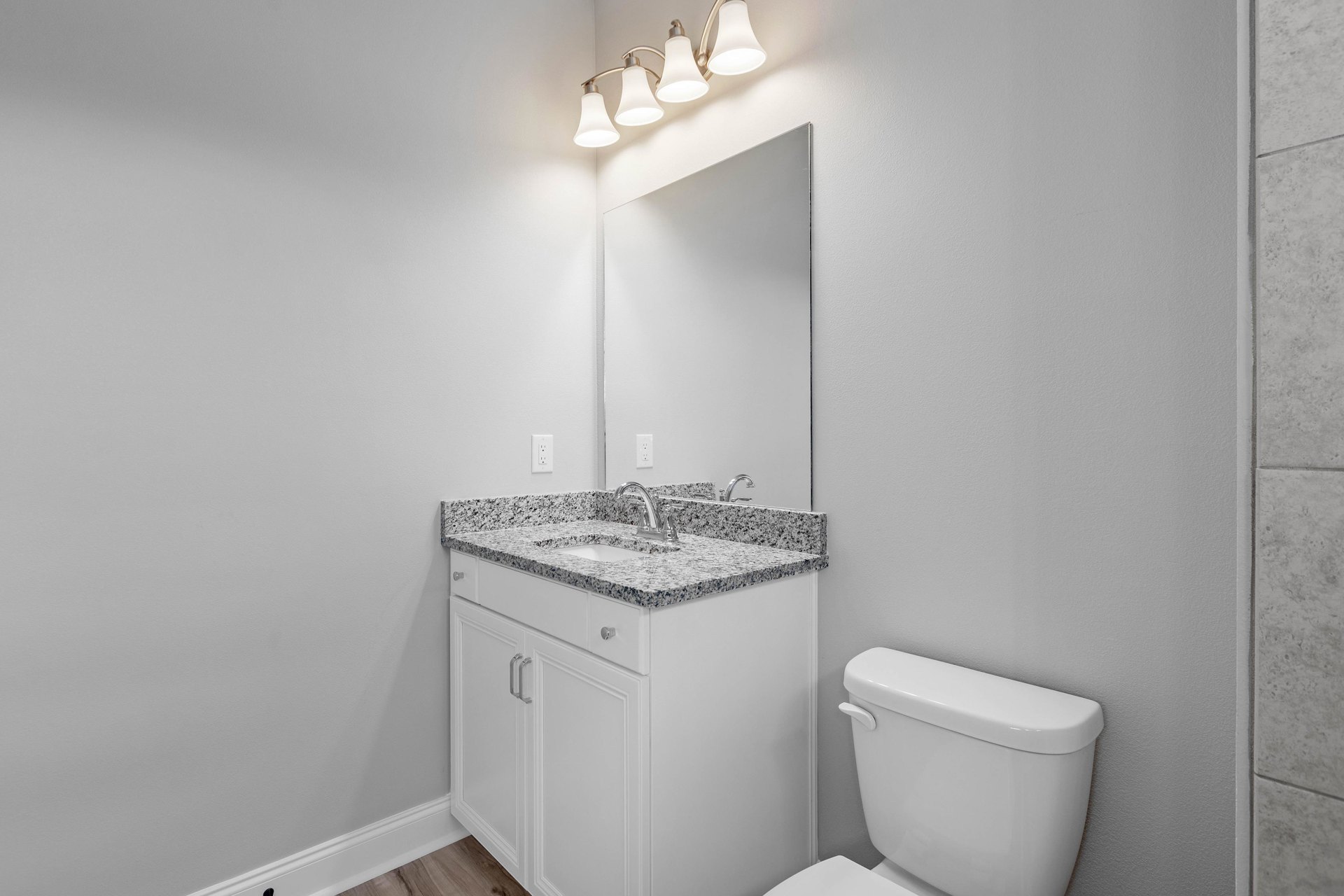 Bathroom with marble countertop, undermount sink, wall-mounted mirror, white toilet, and three-light fixture above the vanity.