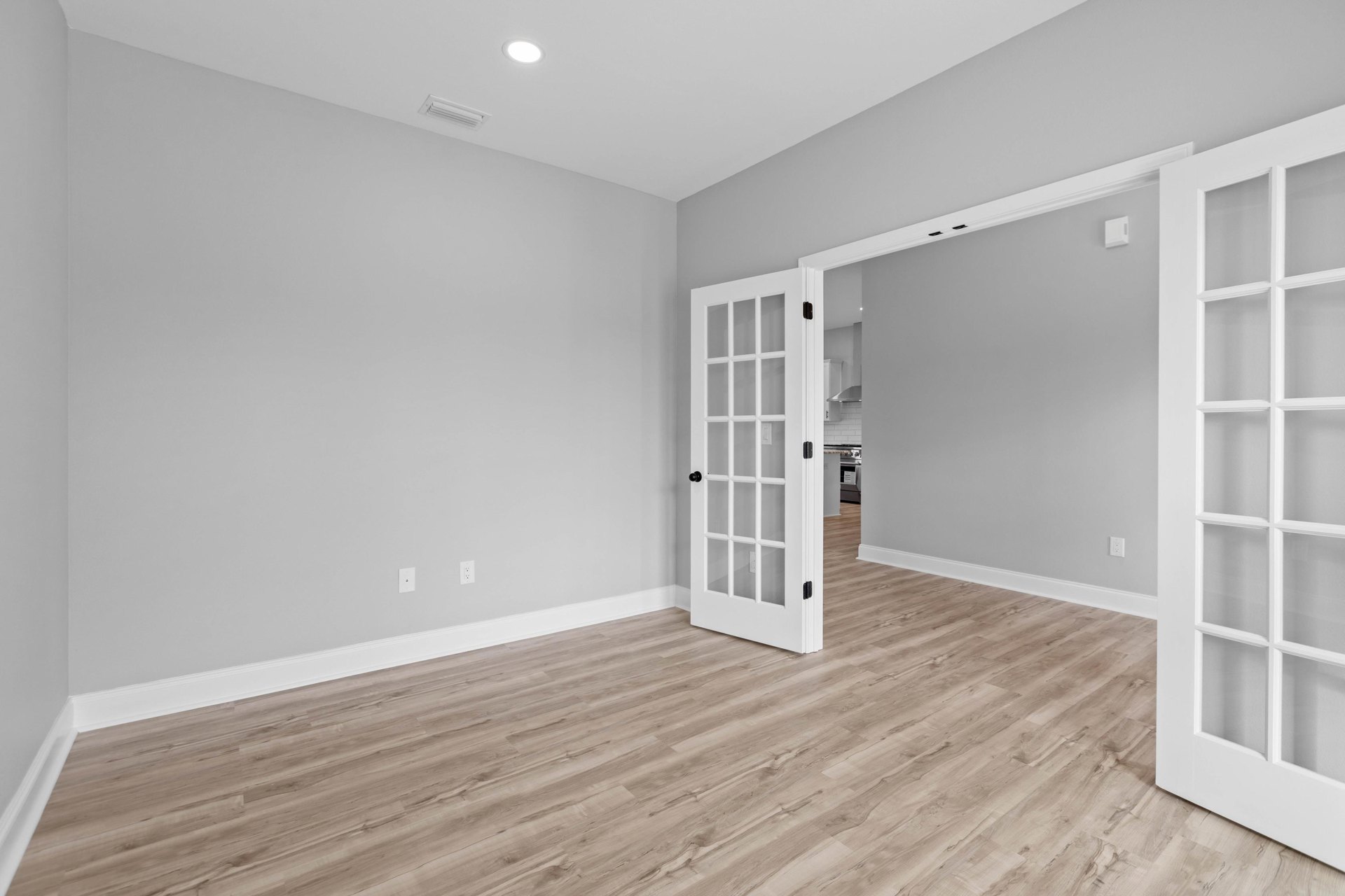 White paneled door with glass panes open to a room with light wood flooring, white walls, and plaster trim