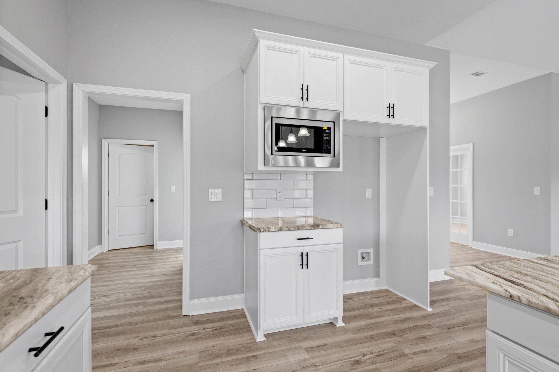 White kitchen with marble countertop, silver microwave built into cabinetry, white door with black knob, bell-shaped pendant light, and close-up of countertop.