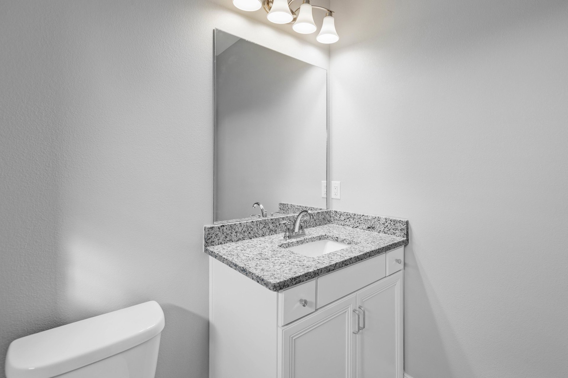 Bathroom with white ceramic sink, chrome faucet, rectangular wall mirror, light-colored tile backsplash, and white cabinetry with drawers.