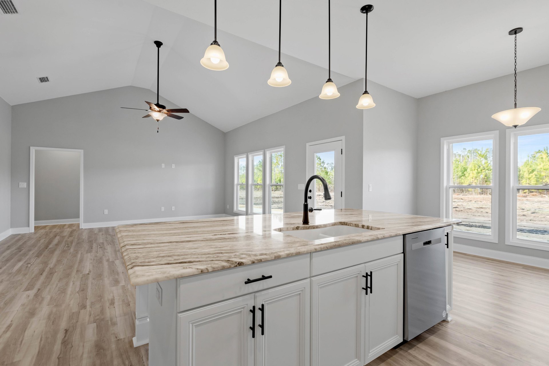 Spacious kitchen featuring a large white island with integrated sink, black accent line on countertop, pendant light fixtures above, white cabinetry, and light wood flooring.