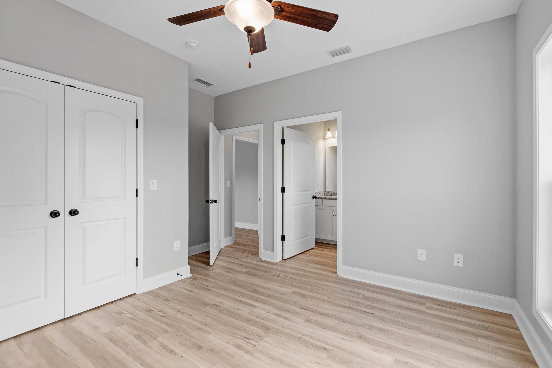 Ceiling fan with light fixture above wood laminate flooring, two white doors with black knobs, neutral walls