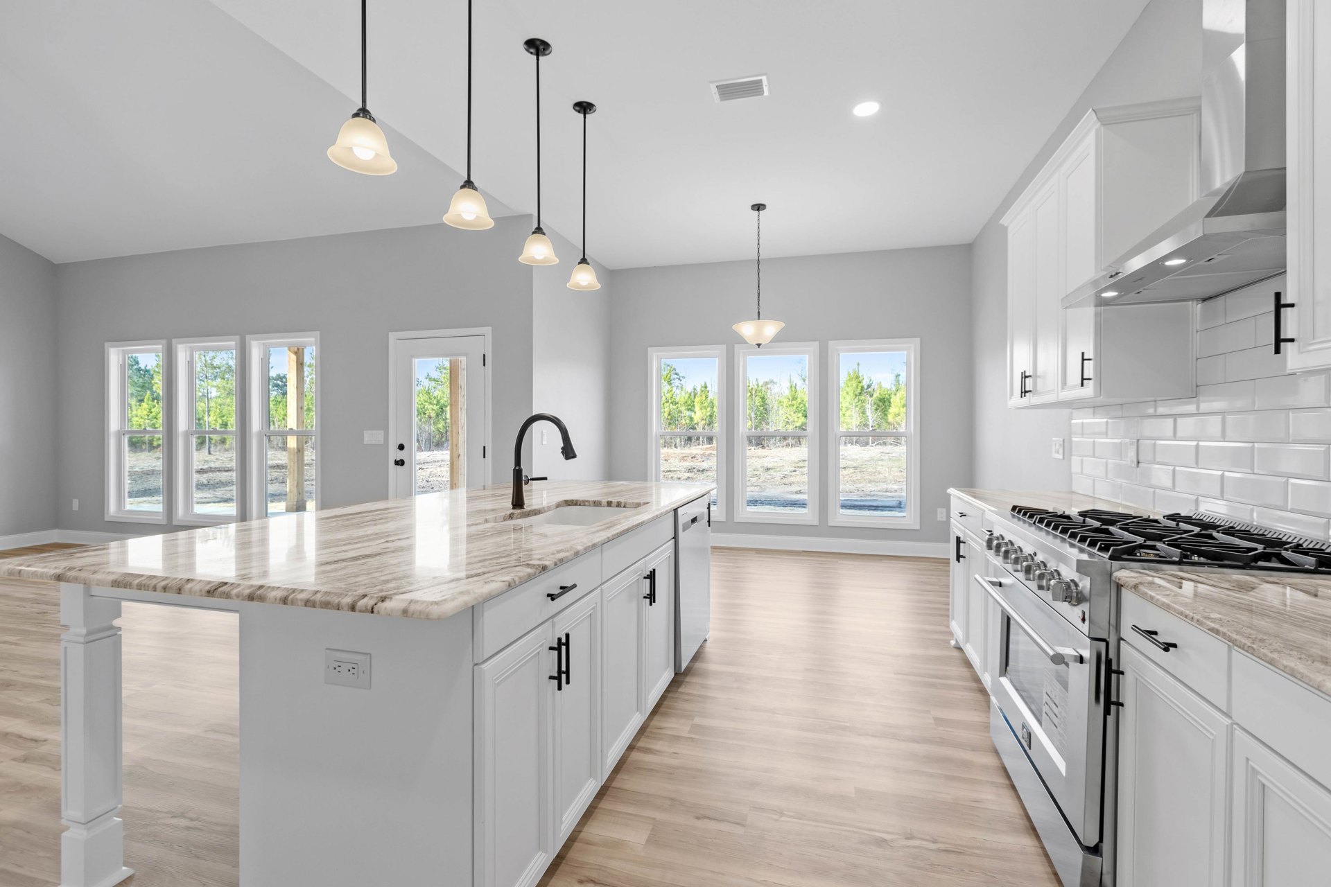 Marble kitchen island with black faucet, white cabinetry, stainless steel stove, recessed ceiling lights, vent hood, and modern light fixture