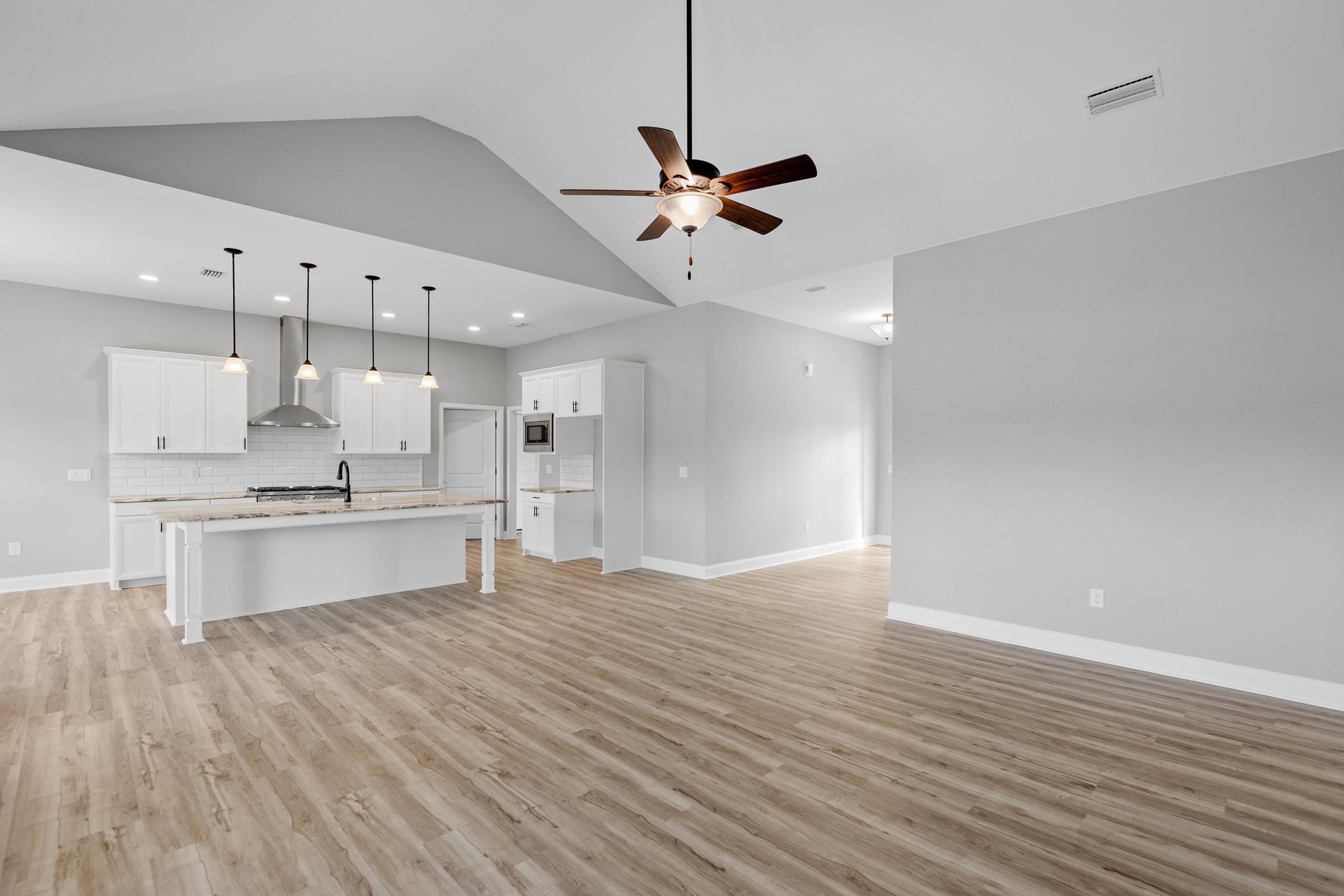 Open-concept kitchen and living room featuring wood flooring, white walls, marble countertop, ceiling fan with light fixture, and vent.