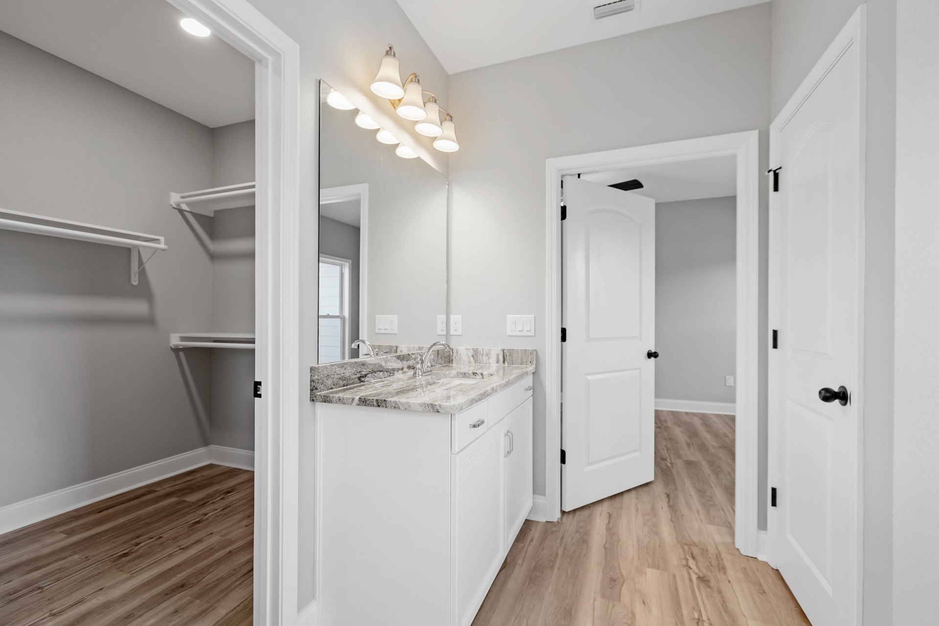 Bathroom featuring a marble countertop sink, wood flooring with white baseboards, white door, wall-mounted mirror, and a row of modern lights above the vanity