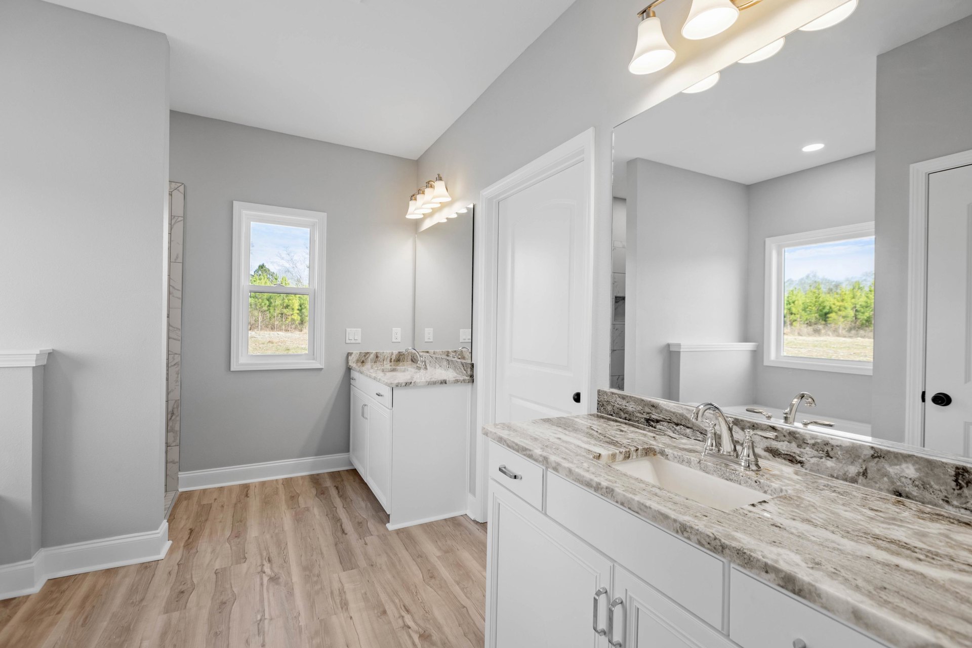 Bathroom with marble countertop, wood flooring, rectangular mirror above sink, and window overlooking trees.