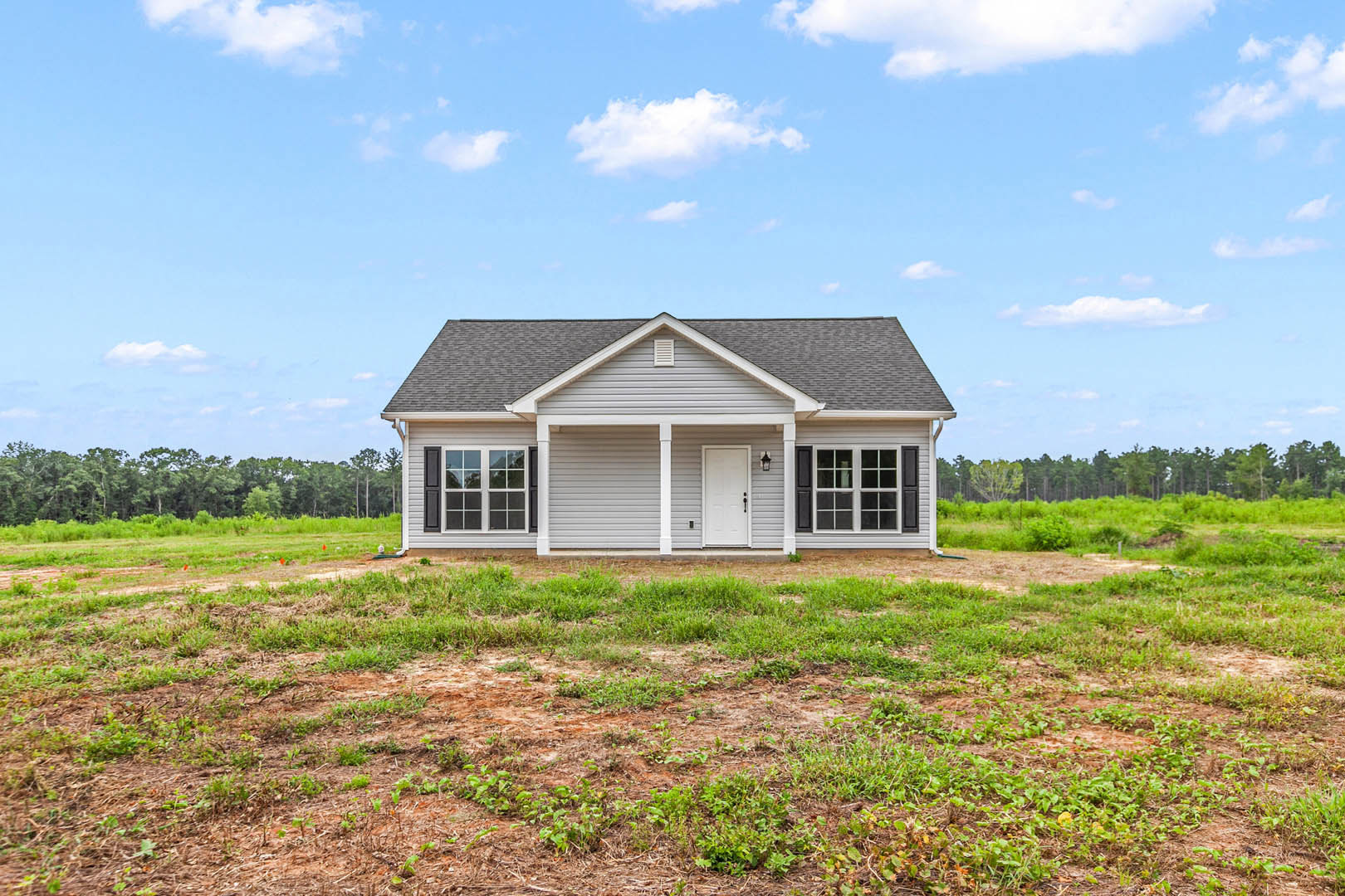 Modern house with black roof, white door, large windows, surrounded by grassy field under blue sky with scattered clouds