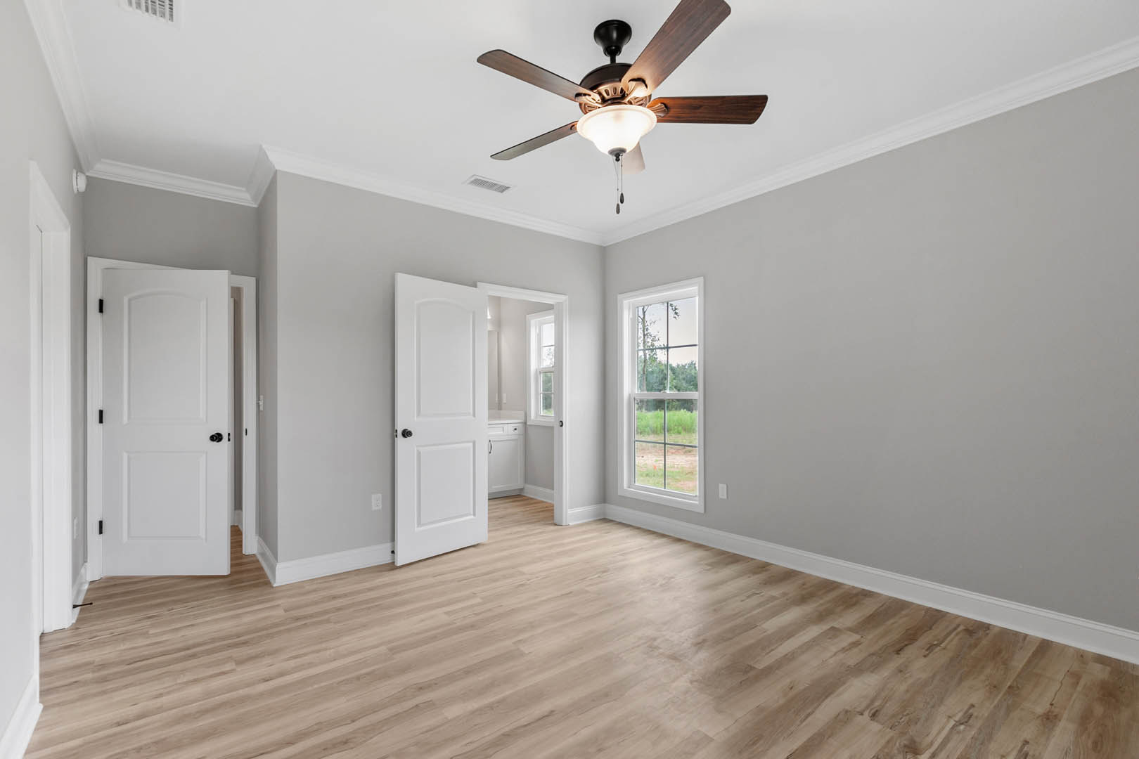 Ceiling fan with light fixture, hardwood floor, white walls, window with outdoor view, white door with black hardware, black lamp shade on white table