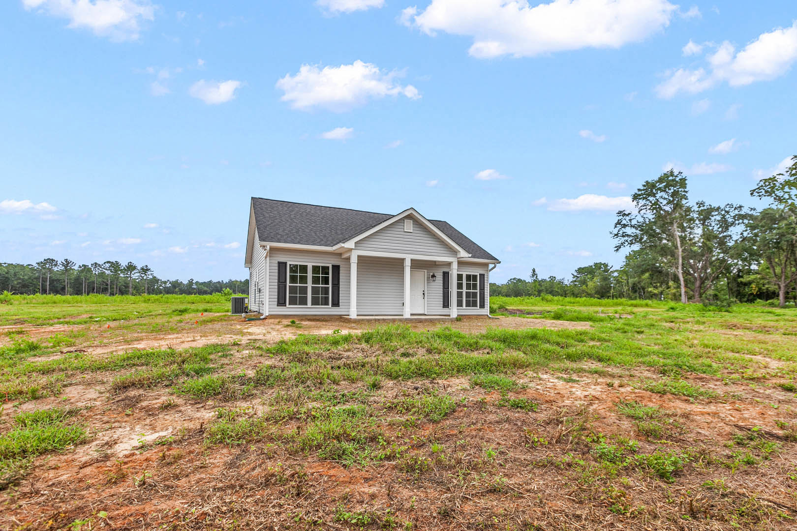 Two-story farmhouse with white trim and covered porch, set in a grassy field under a blue sky with scattered clouds