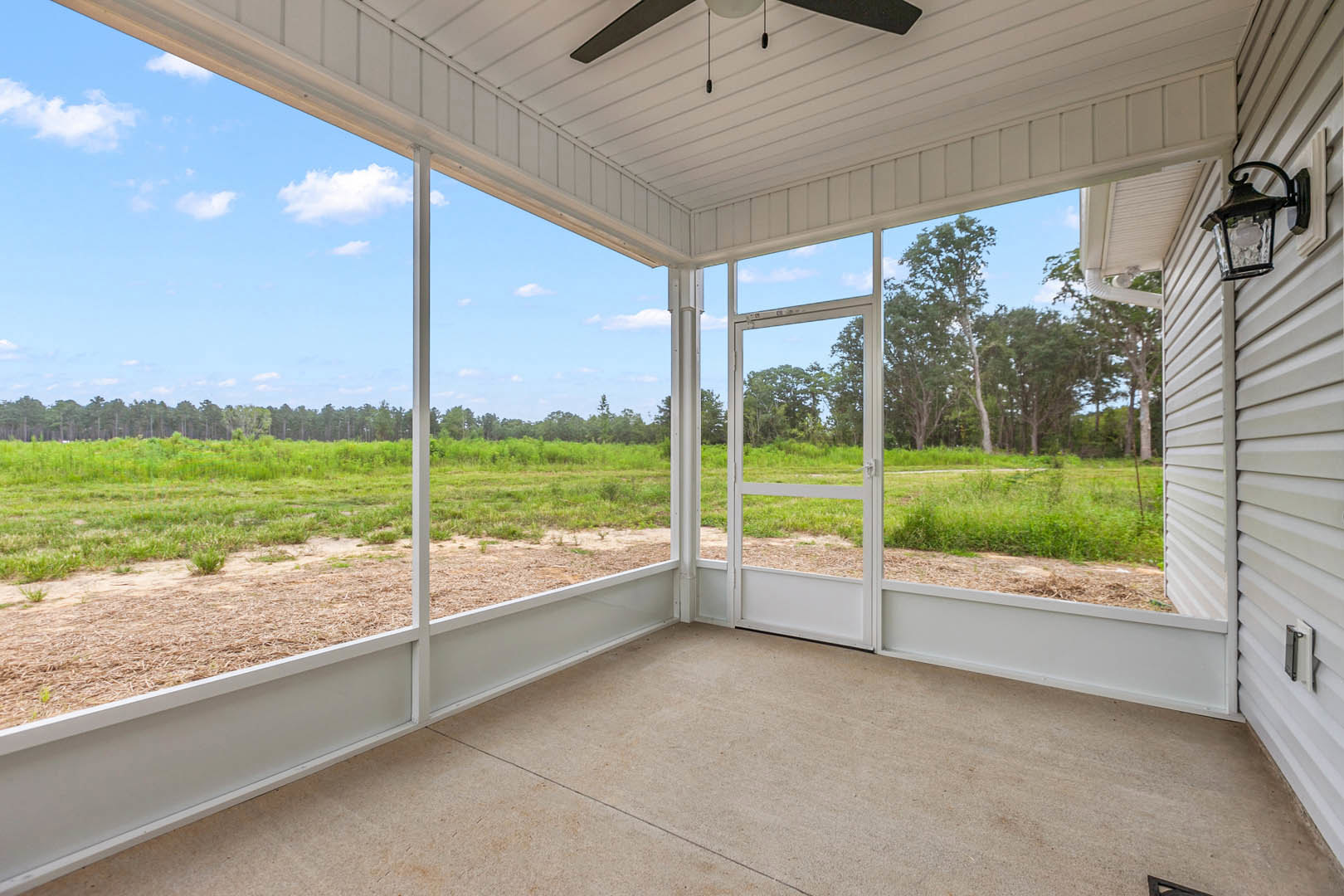 Open-concept room with polished concrete floor, large white-framed windows overlooking grassy field and trees, ceiling fan, modern lamp, and black pendant light fixture