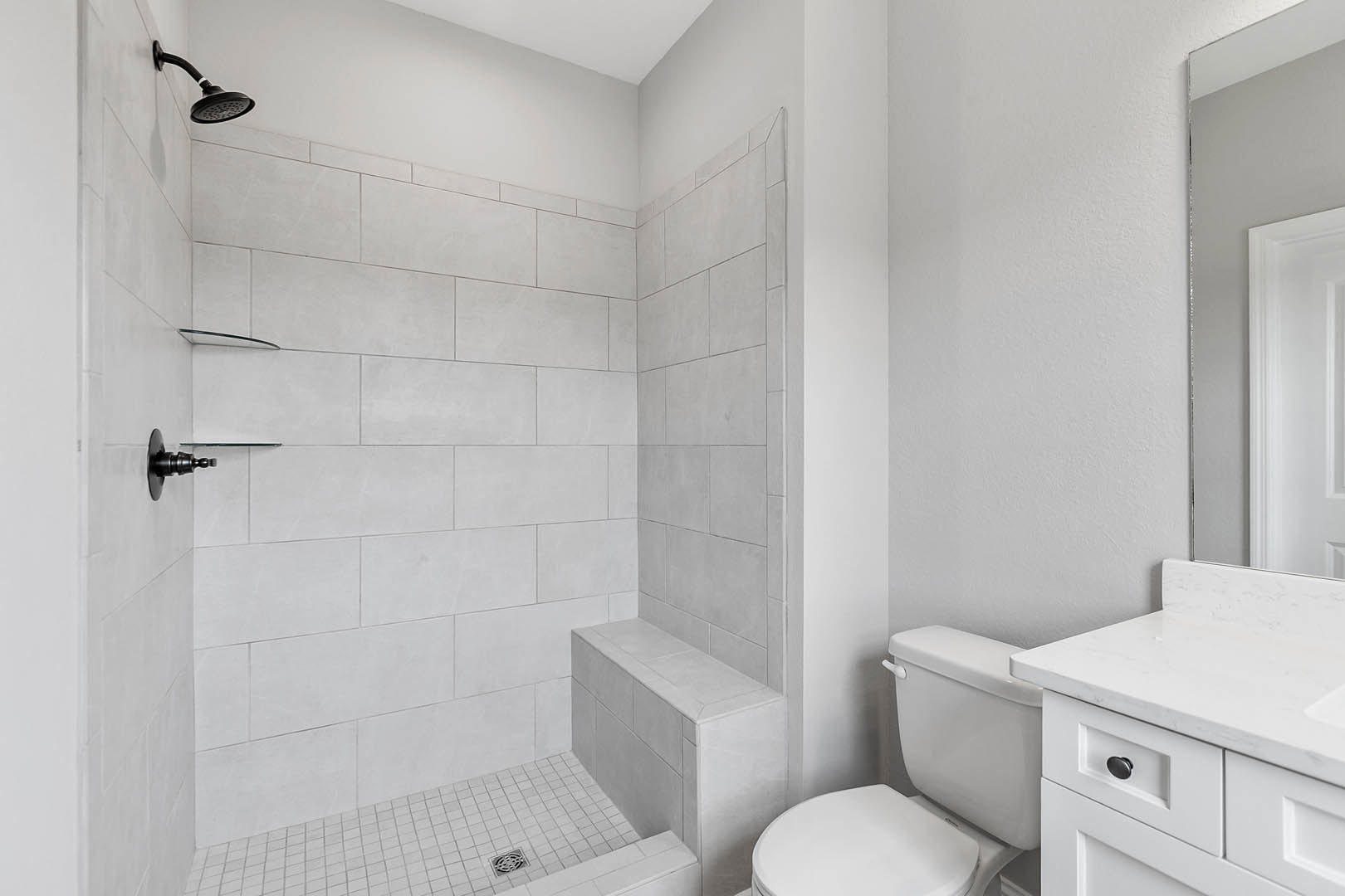 Modern bathroom with white countertop, wall-mounted shower head, black metal towel bar, tiled walls, and toilet adjacent to bathtub