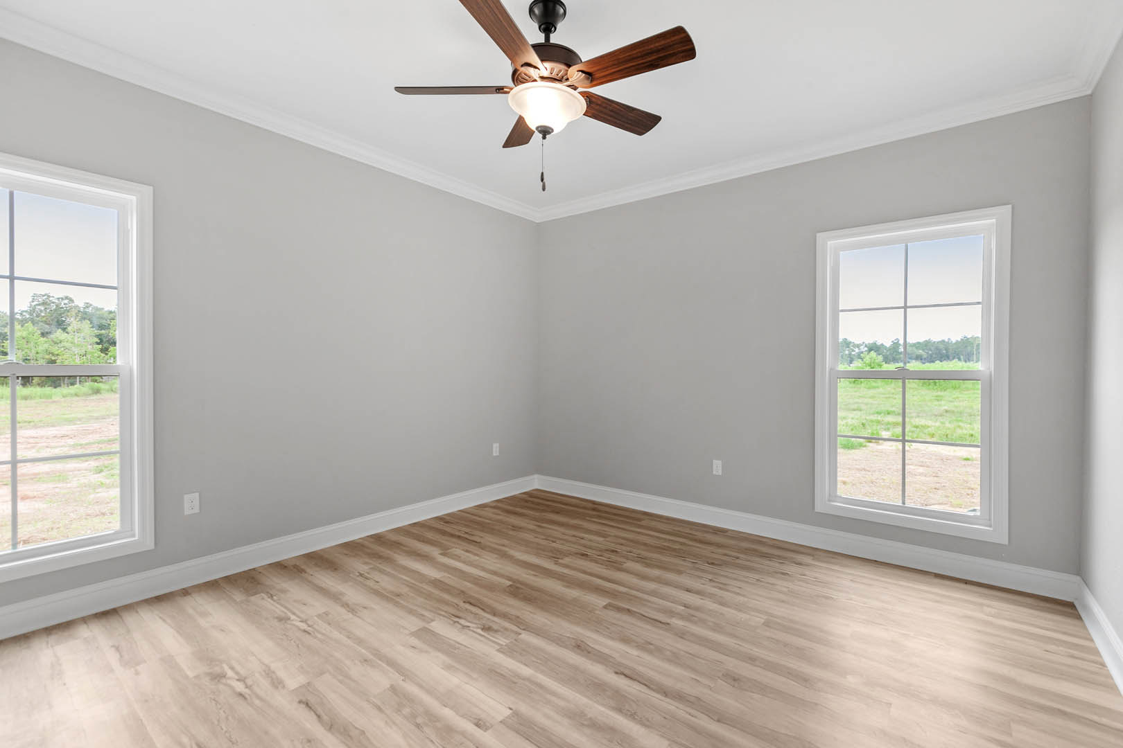 Ceiling fan with light fixture above wood floor and white baseboards, large window showing grassy field and trees, black lamp in foreground