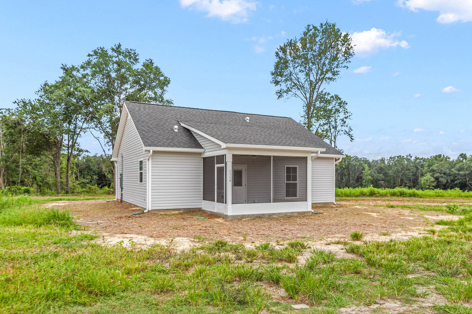 Two-story home with gray siding, covered front porch supported by white columns, white-framed windows, white front door with glass panel, manicured grass lawn, and gabled roof
