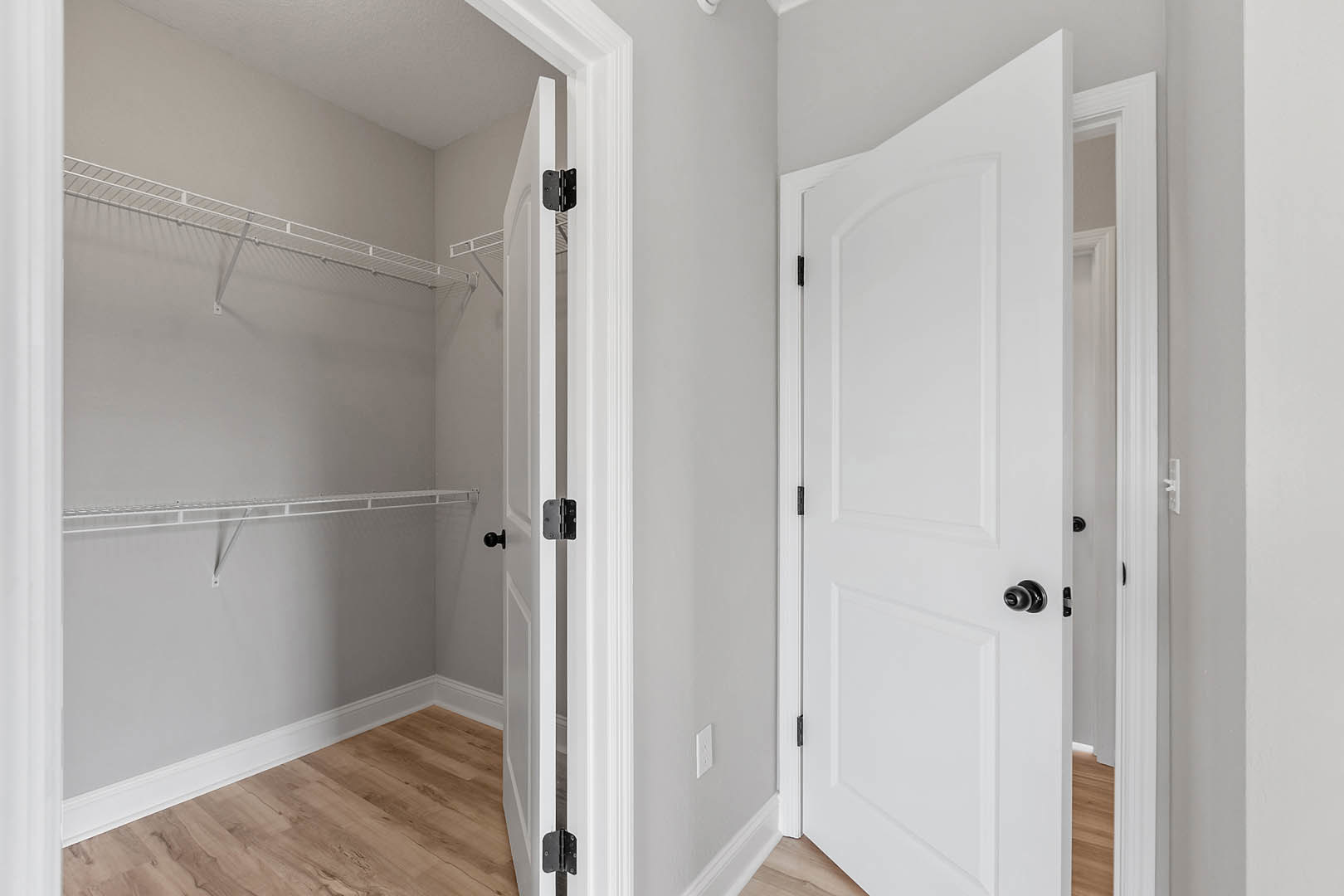 Closet with white paneled doors, black handles, built-in white shelves, wood flooring, and white baseboards