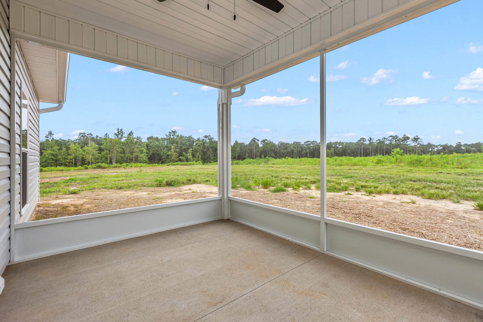 Open-concept room with polished concrete floor, large white-framed window overlooking grassy field and trees, white ceiling with modern fan