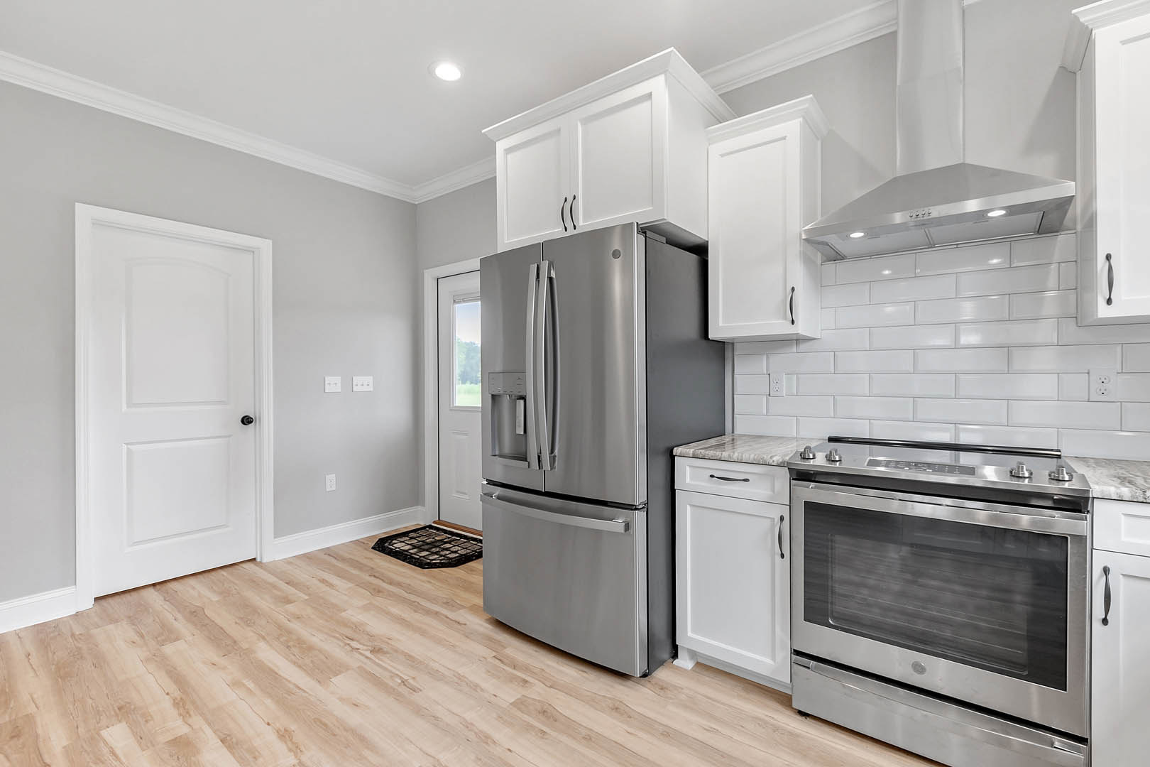 Modern kitchen featuring stainless steel refrigerator and oven with glass door, white cabinetry, black hardware, light countertops, and wood flooring