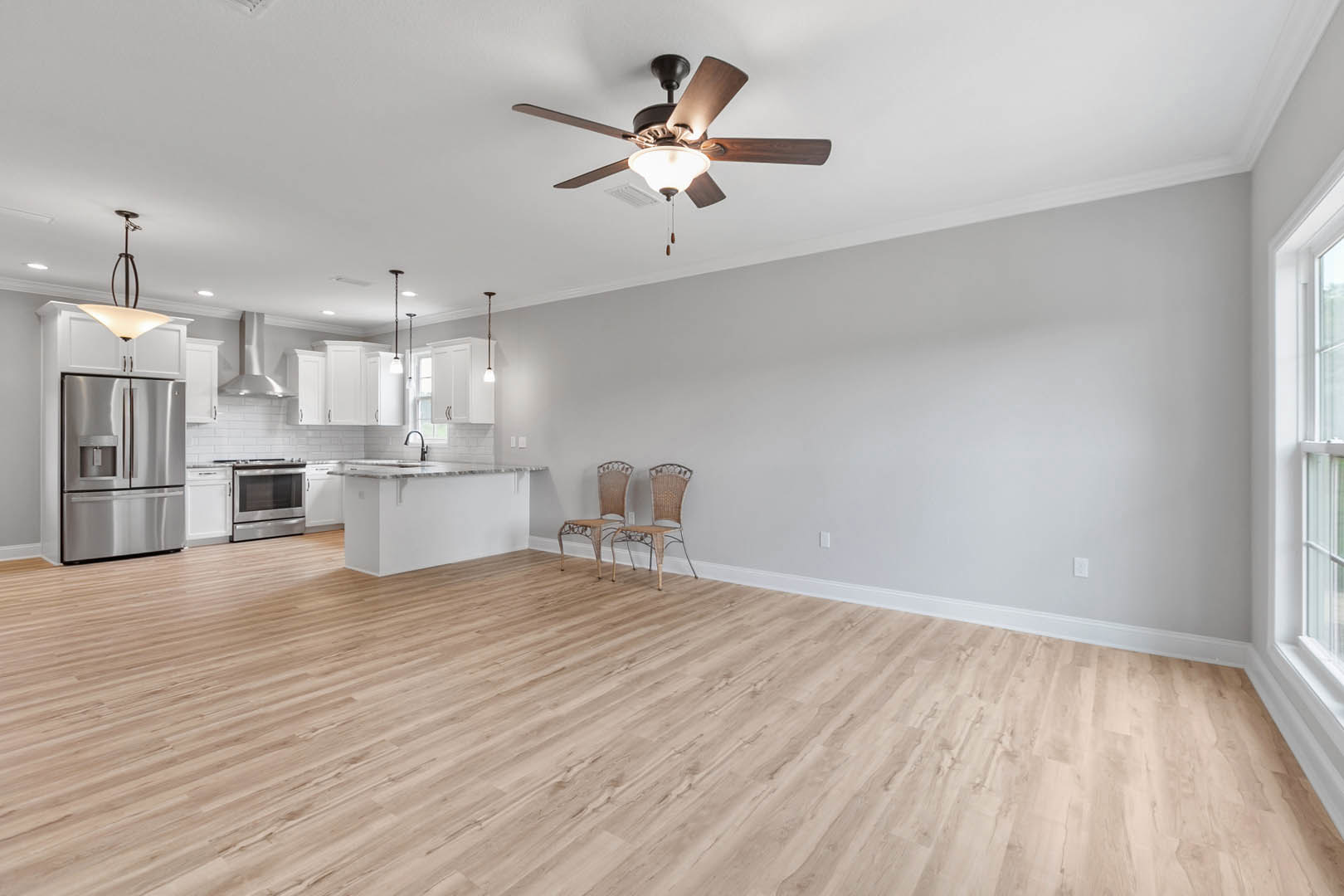 Open-concept kitchen with stainless steel refrigerator and oven, wood flooring, ceiling fan with light fixture, wicker chair in corner, neutral walls