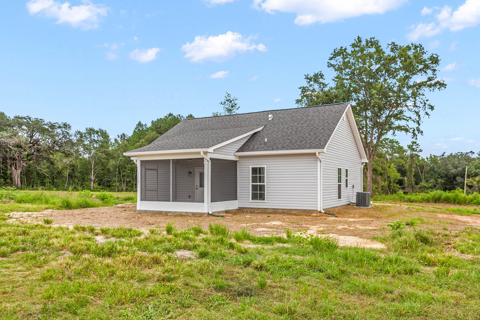 Two-story house with white door and window, surrounded by lush green grass and mature trees, grey metal object on lawn, cloudy sky overhead