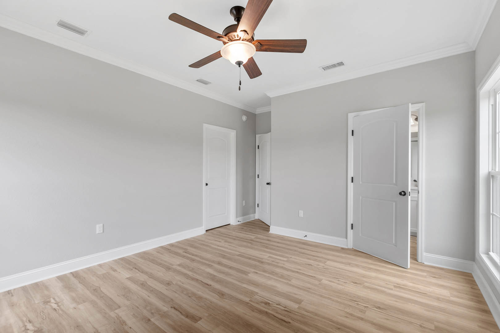 Ceiling fan with light fixture above wood flooring, white walls, and two white doors with black knobs and white trim
